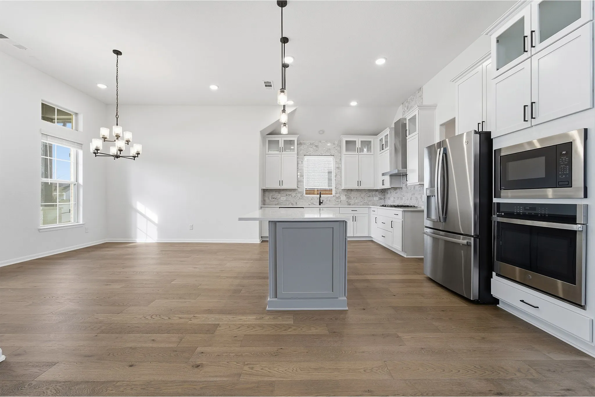 Open-concept living space featuring wood-finish flooring, a contemporary chandelier, and a kitchen with a light gray island, white cabinetry, and stainless steel appliances