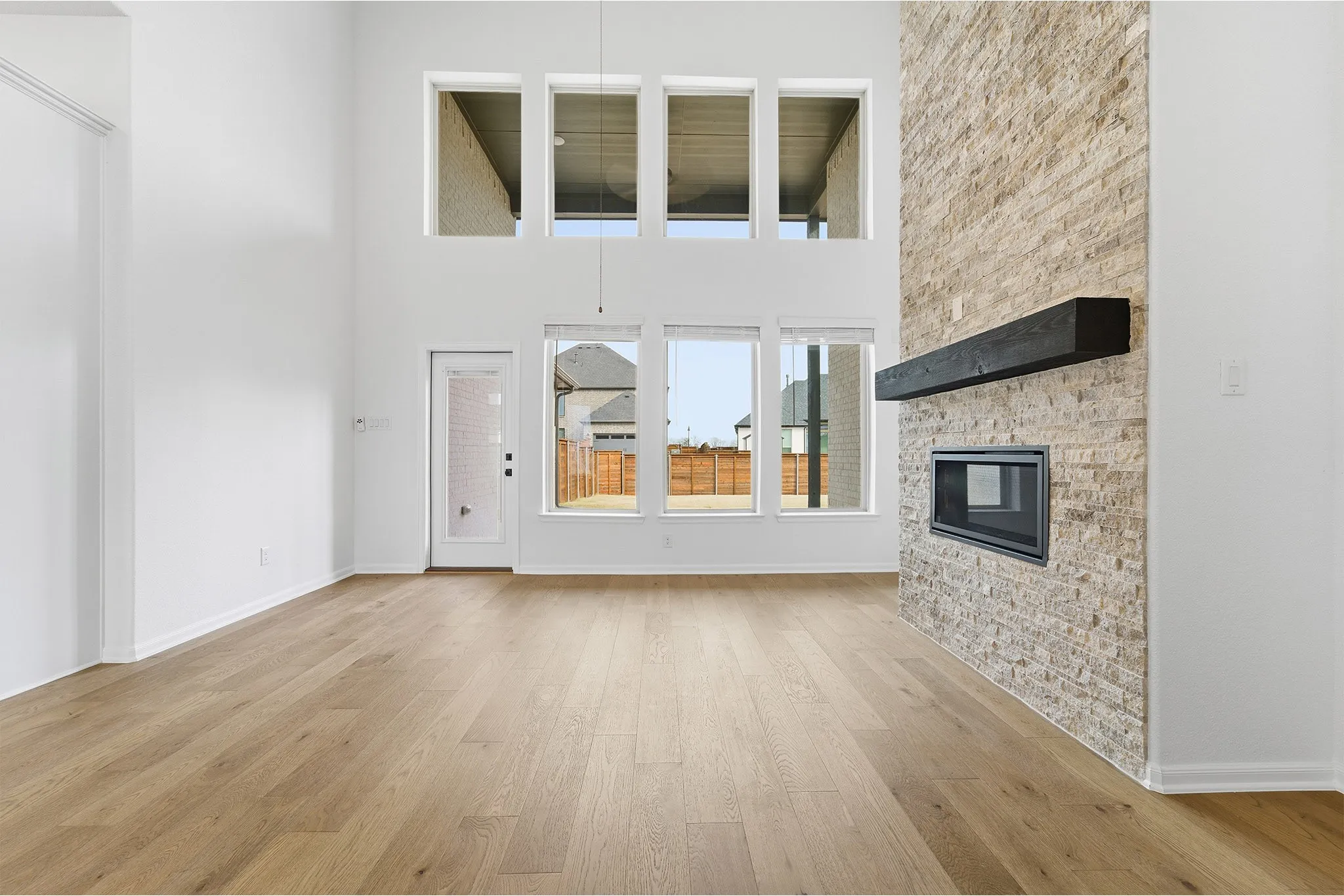 Spacious living area featuring high ceilings, light wood-finish flooring, and multiple windows
