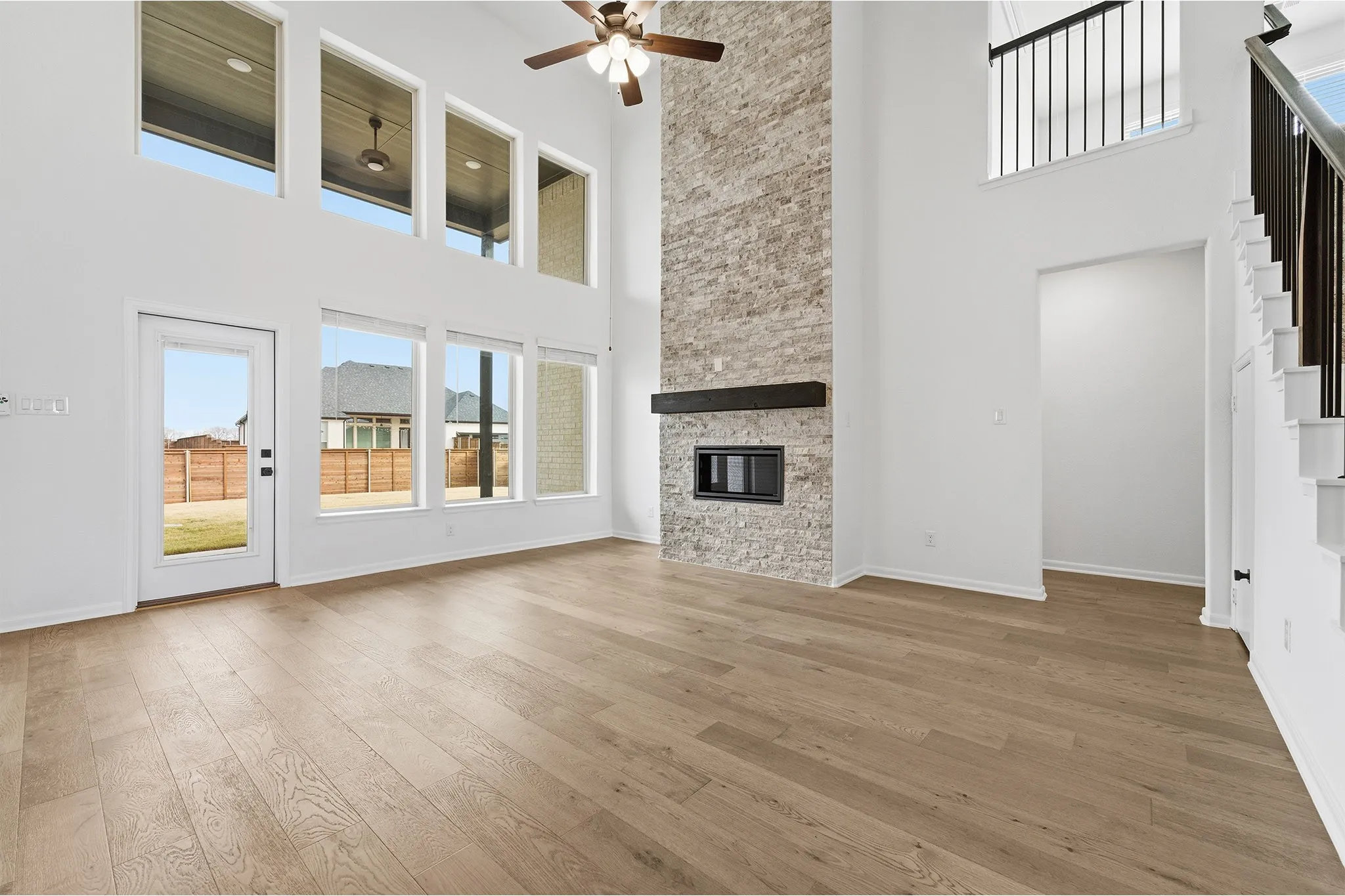 Spacious living area featuring high ceilings, wood-finish flooring, a stacked stone fireplace with a dark wood mantel, and a multi-pane glass door providing exterior access