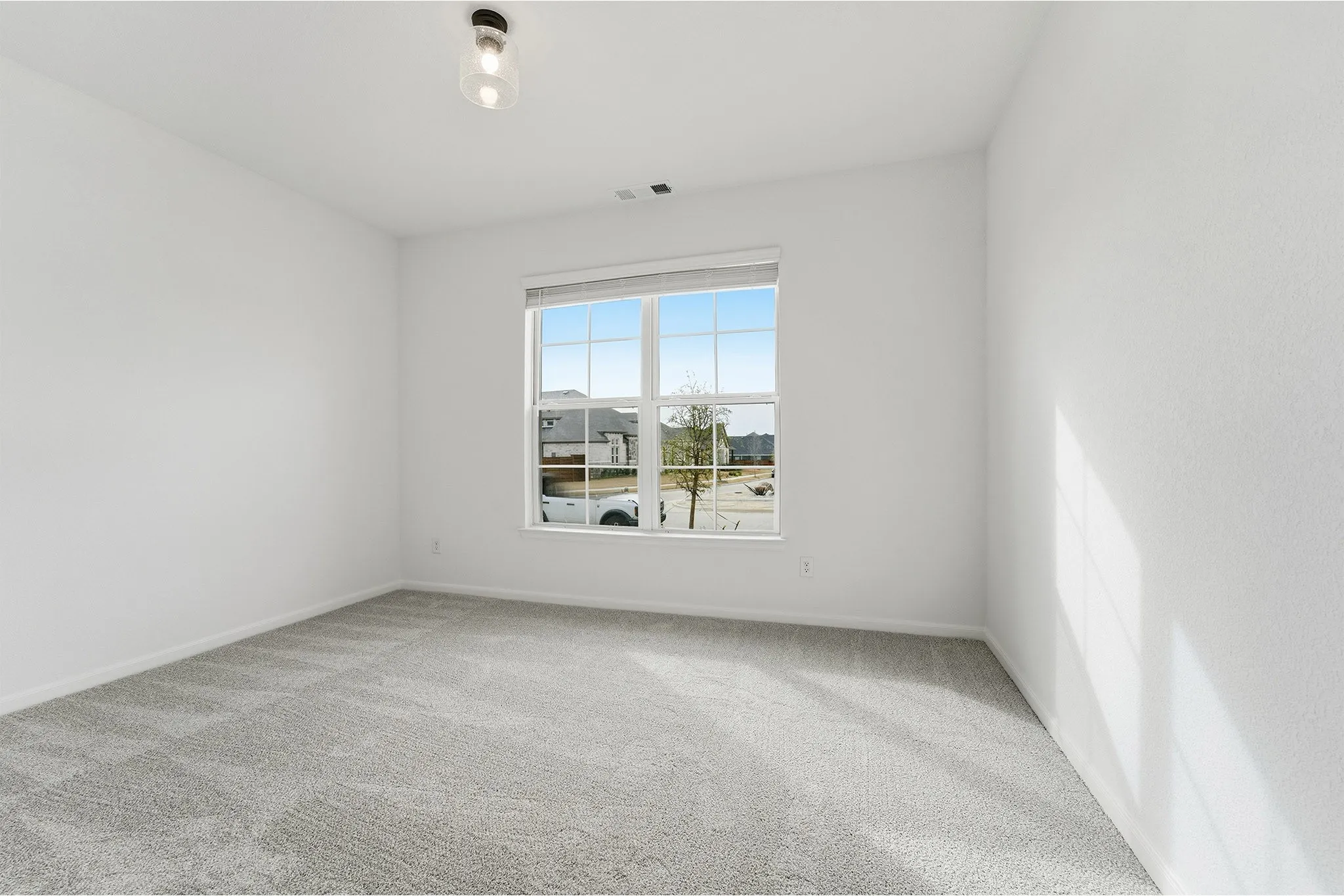 Bright room featuring a large window, neutral gray carpet, white walls, and a modern ceiling light fixture