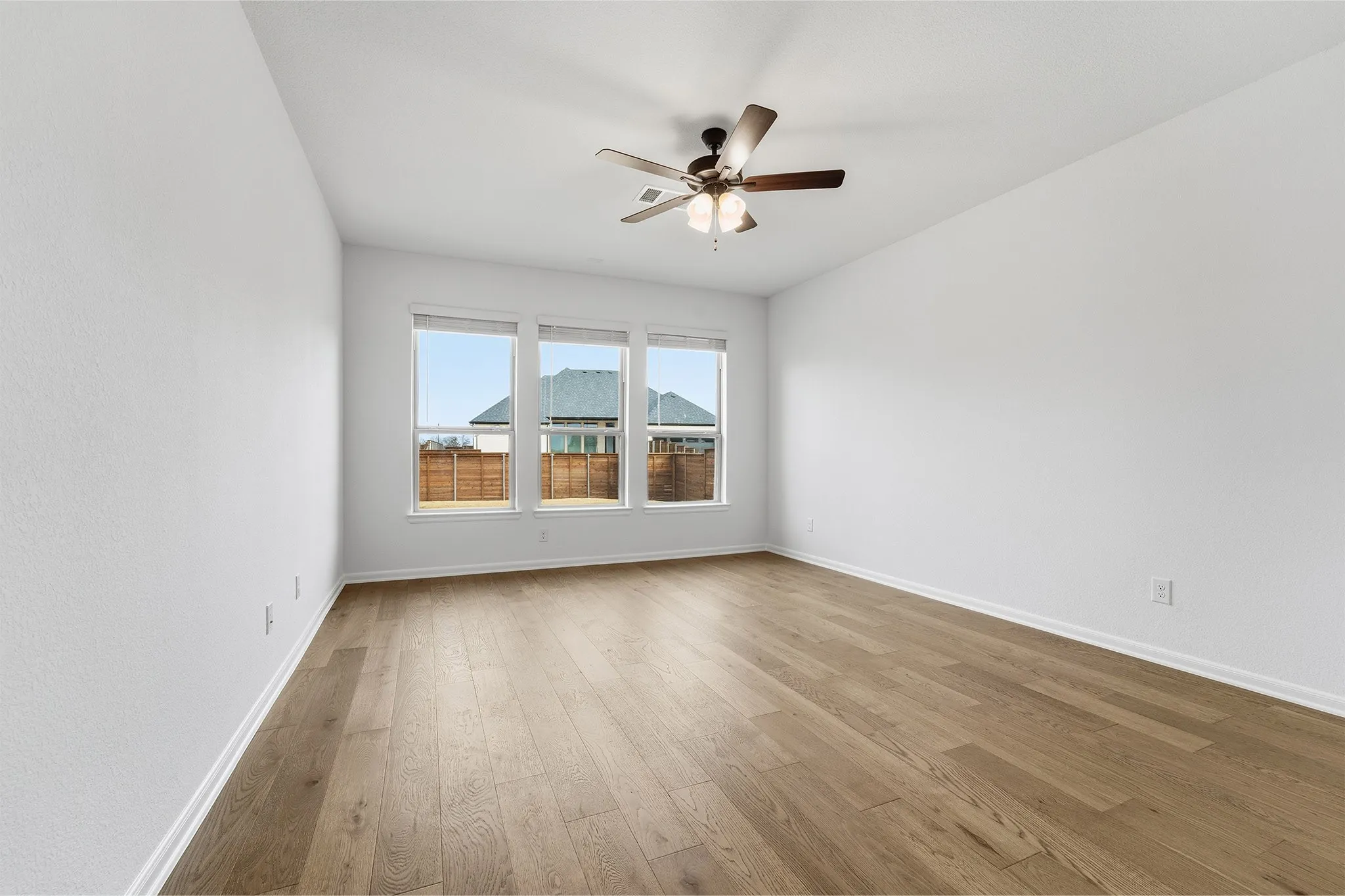 Bright interior space with wood-finish flooring, white walls, and a ceiling fan with integrated lighting