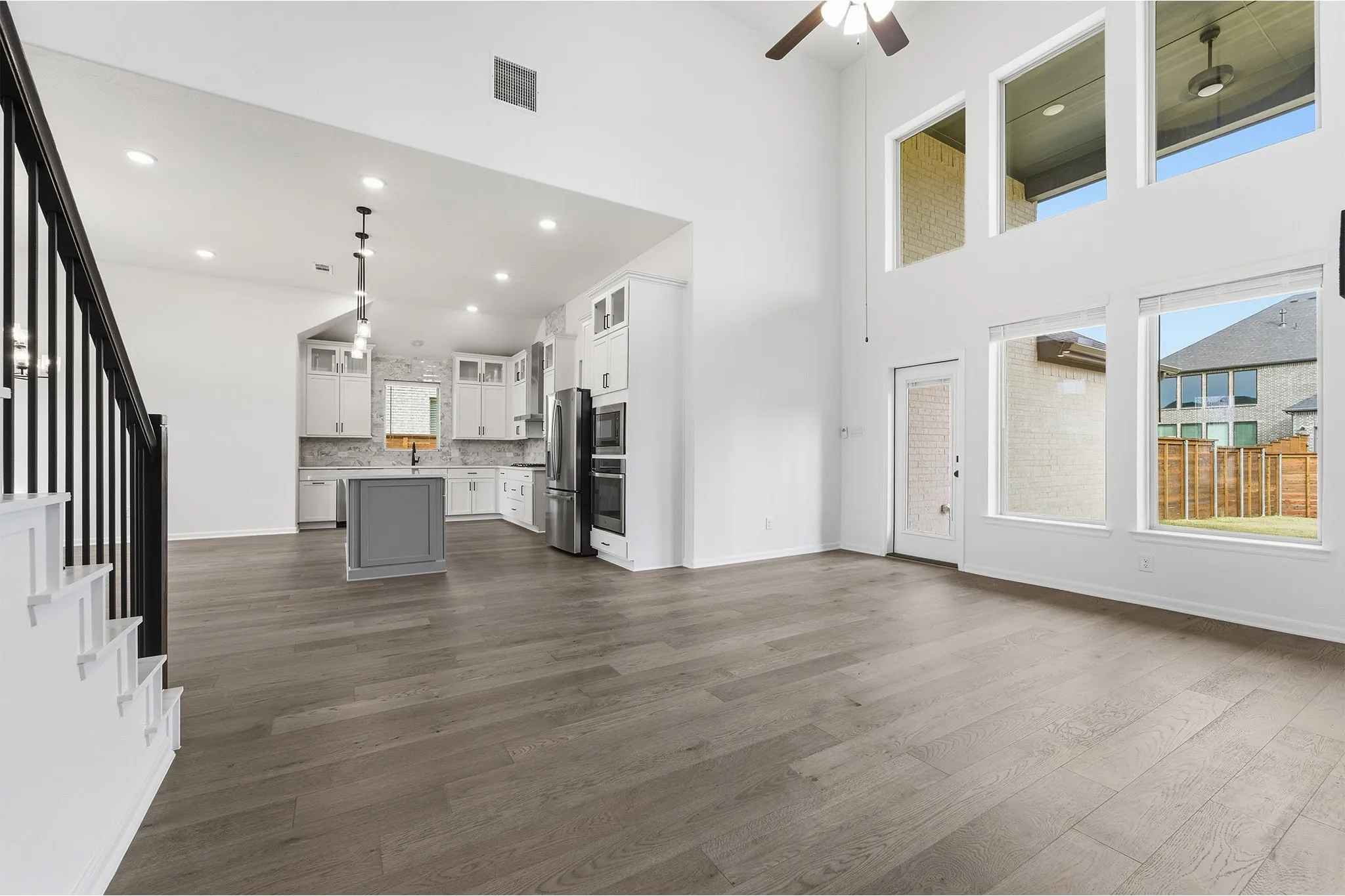 Open-concept living space featuring wood-finish flooring, a two-story ceiling, and abundant natural light from multiple large windows