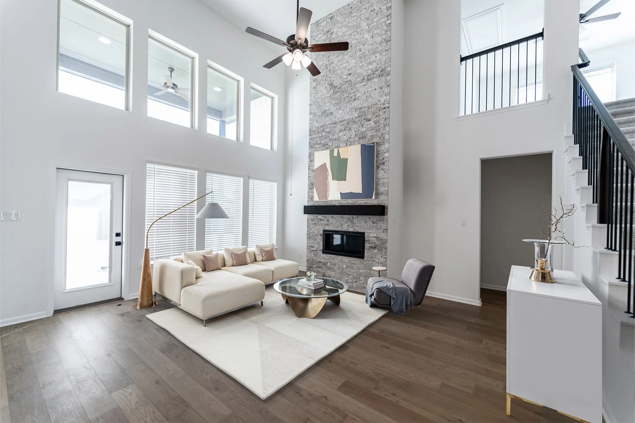 Vaulted living area featuring a floor-to-ceiling stone-clad fireplace with a built-in linear electric firebox, extensive window placements, and wood-finish flooring