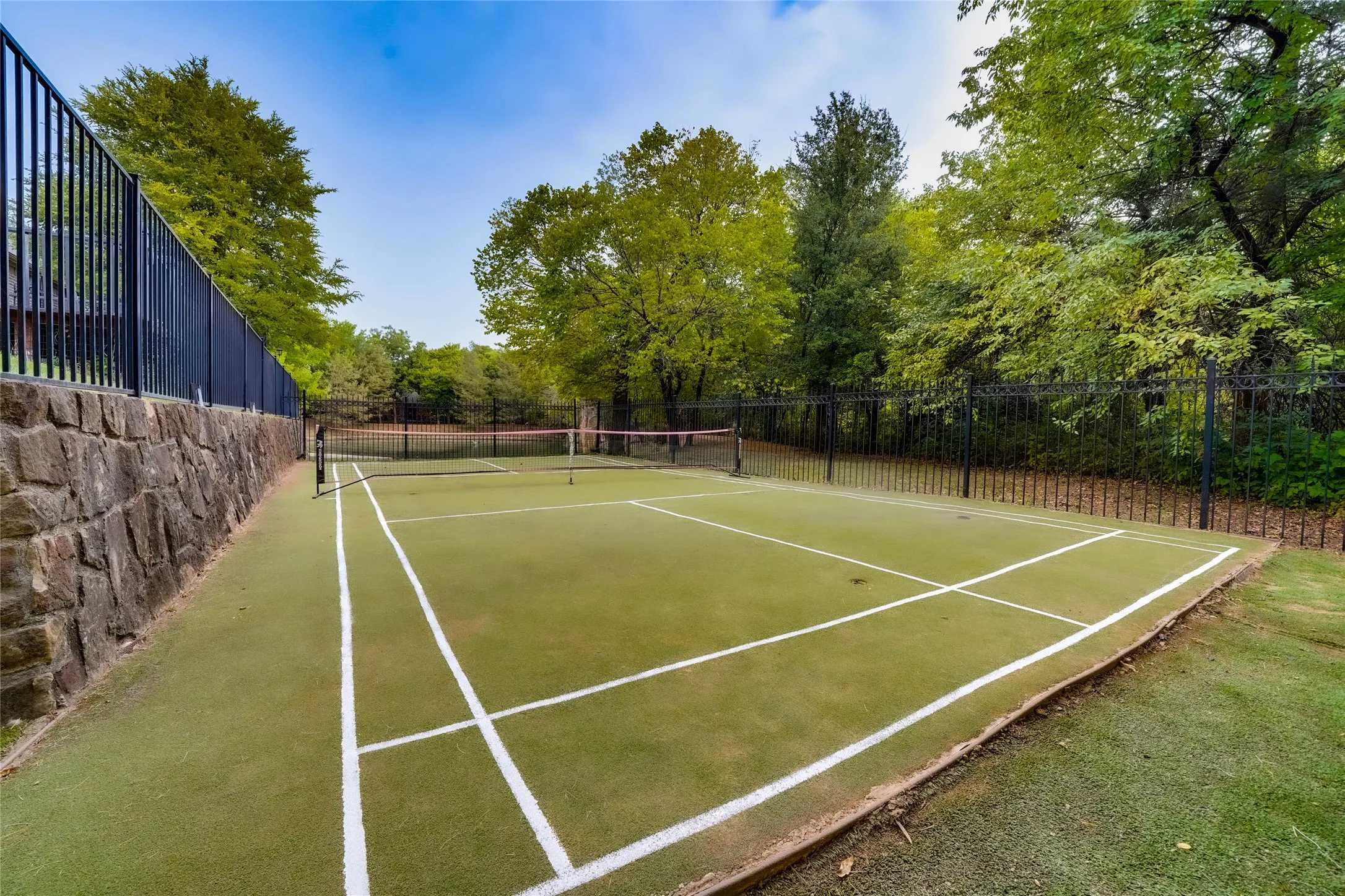 Multi-sport court with perimeter fencing, net system, and a stone retaining wall