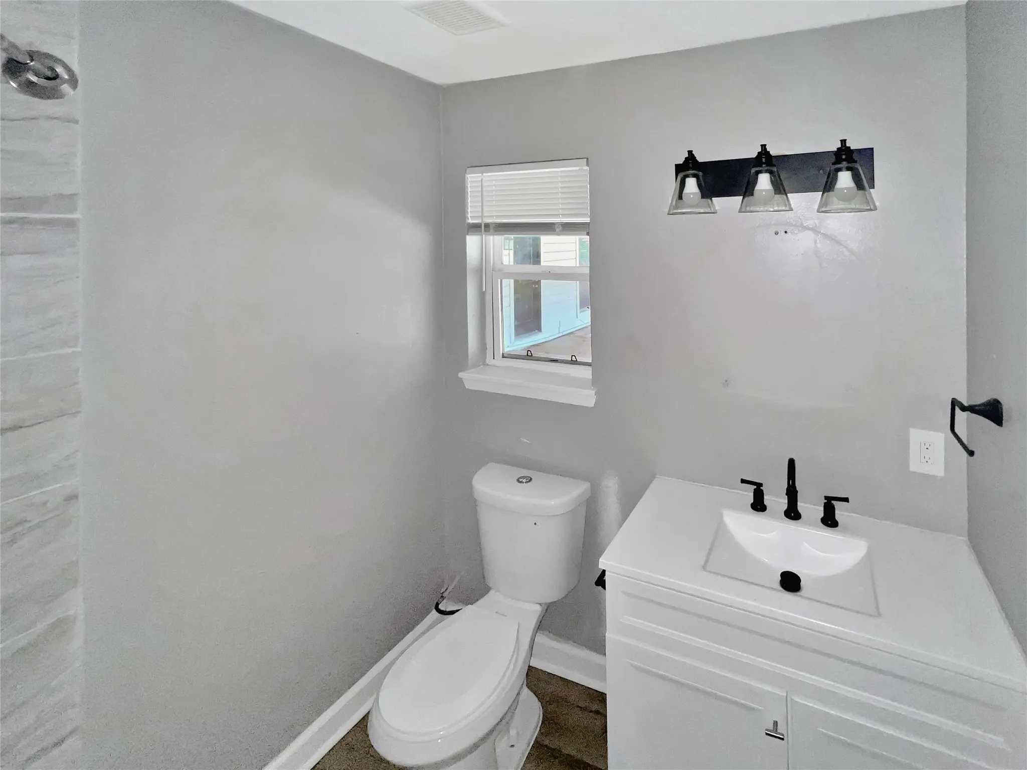 Contemporary bathroom featuring a white vanity with integrated sink, black fixtures, and a three-light vanity bar