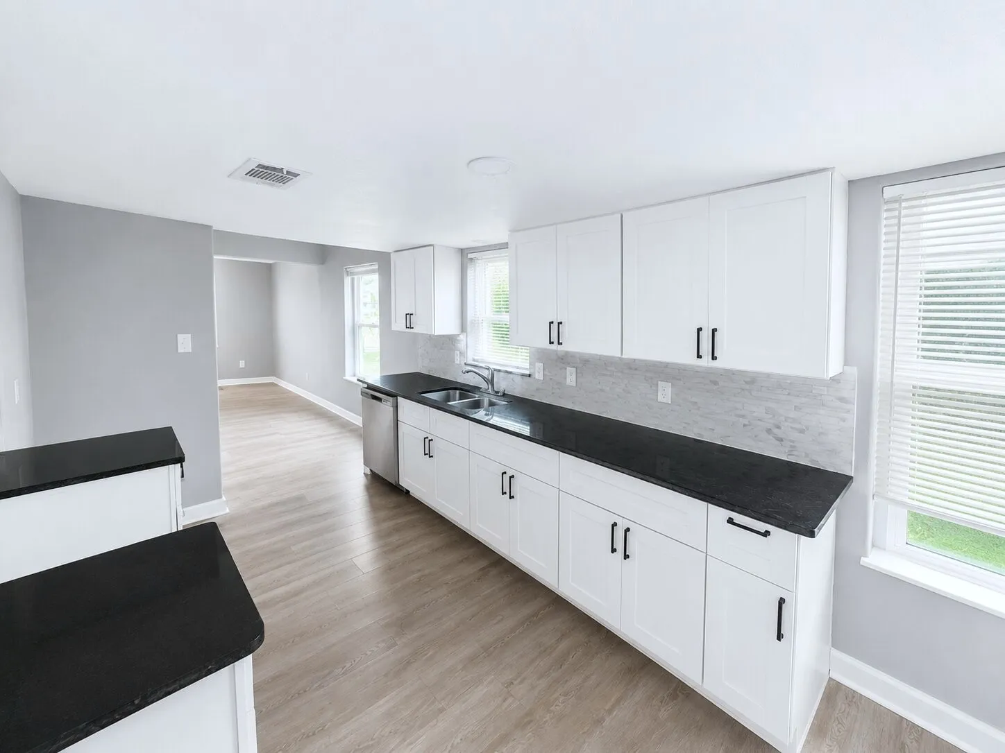 Kitchen featuring white shaker-style cabinetry with black hardware, dark countertops, and a light-toned tile backsplash