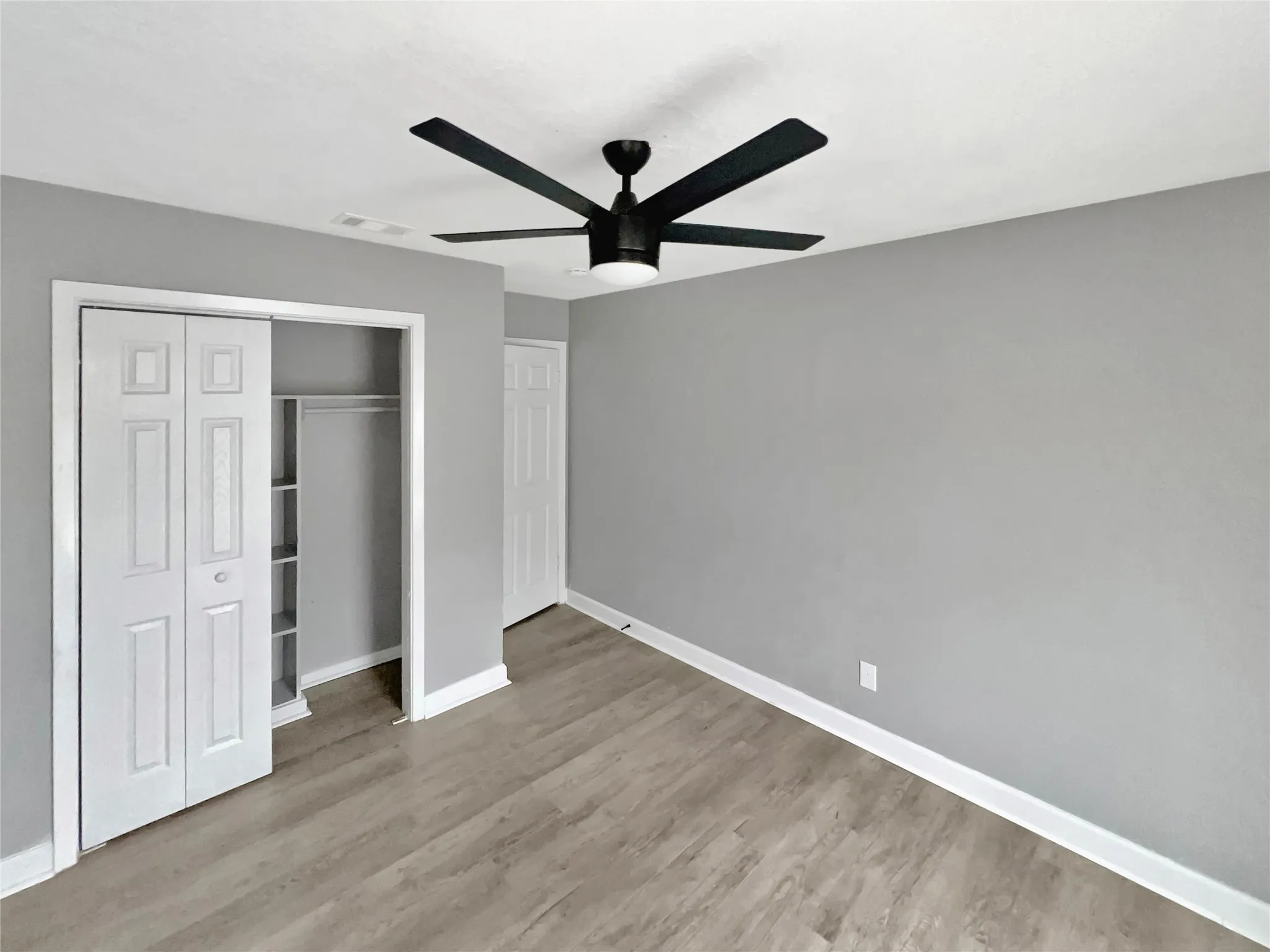 Room featuring light gray walls, wood-finish flooring, and a contemporary black ceiling fan with integrated lighting