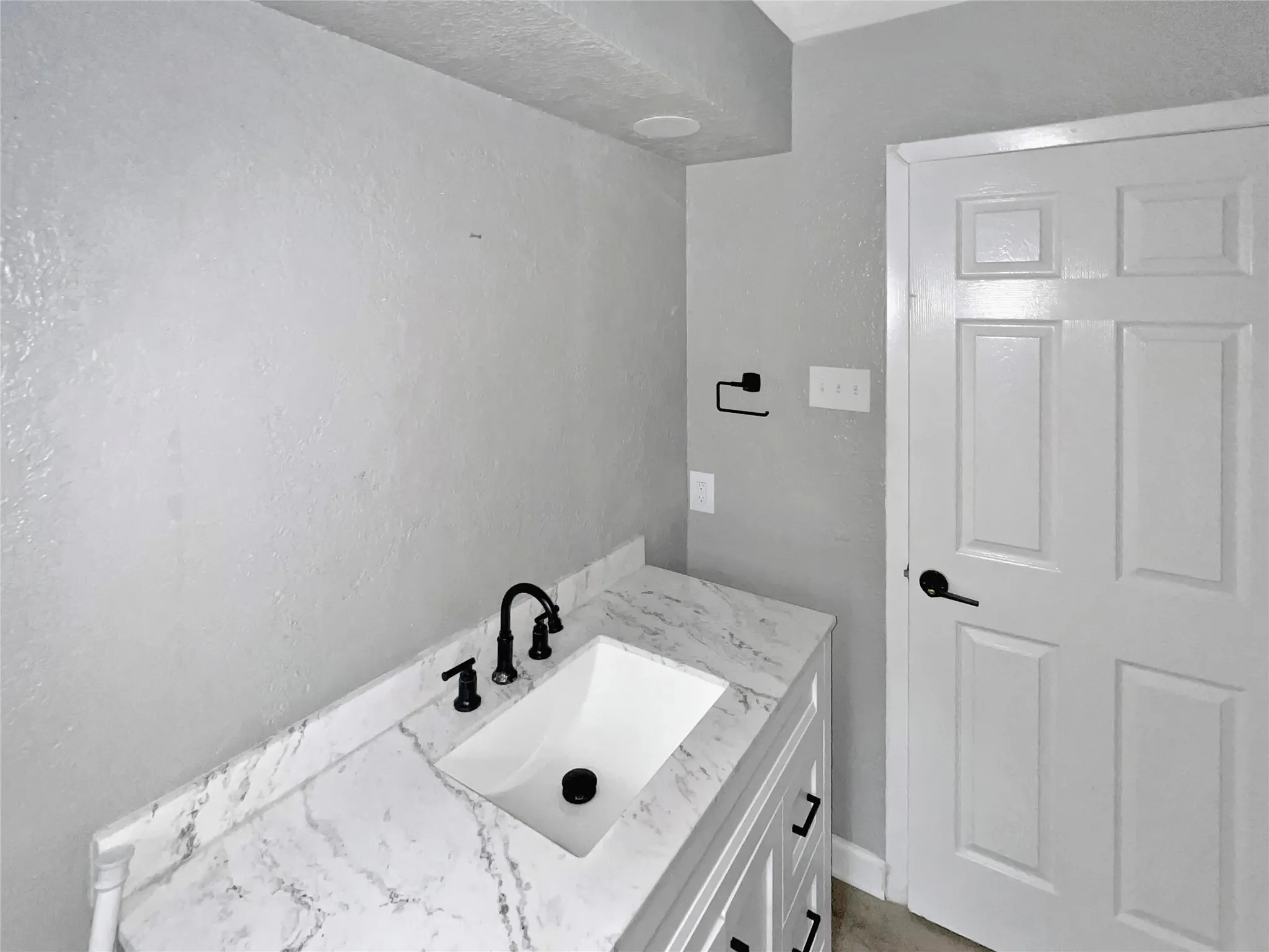 White vanity featuring a built-in rectangular sink, black hardware, and a stone-finish countertop