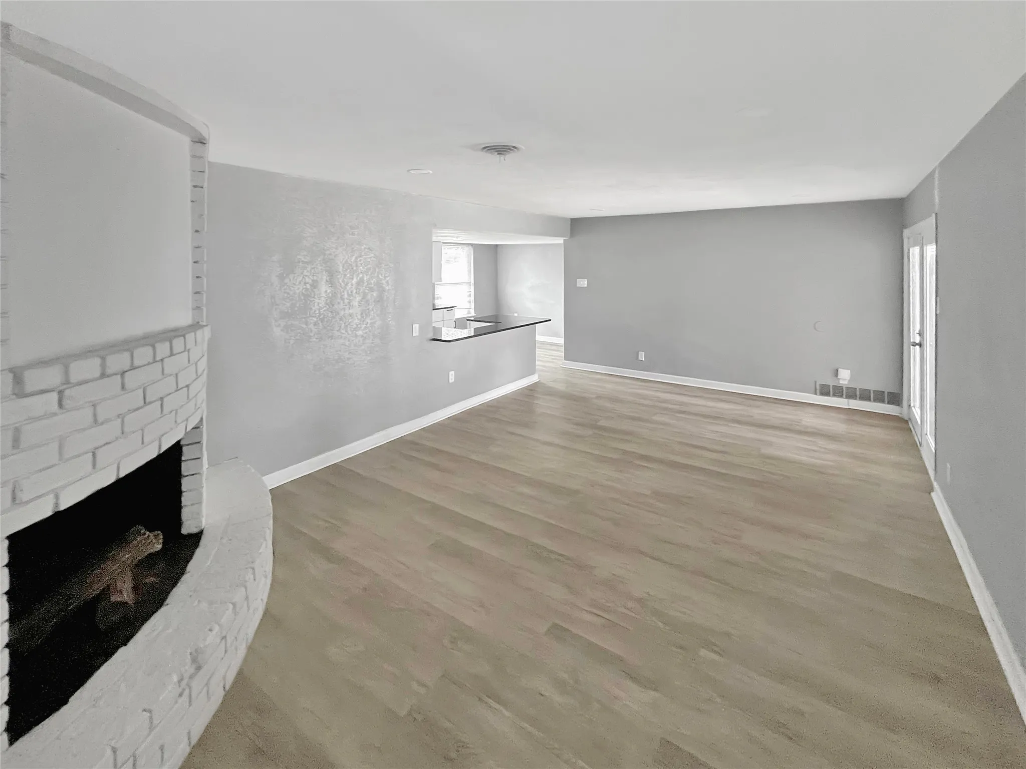 Spacious living area featuring a curved brick fireplace, wood-finish flooring, and a contemporary color palette