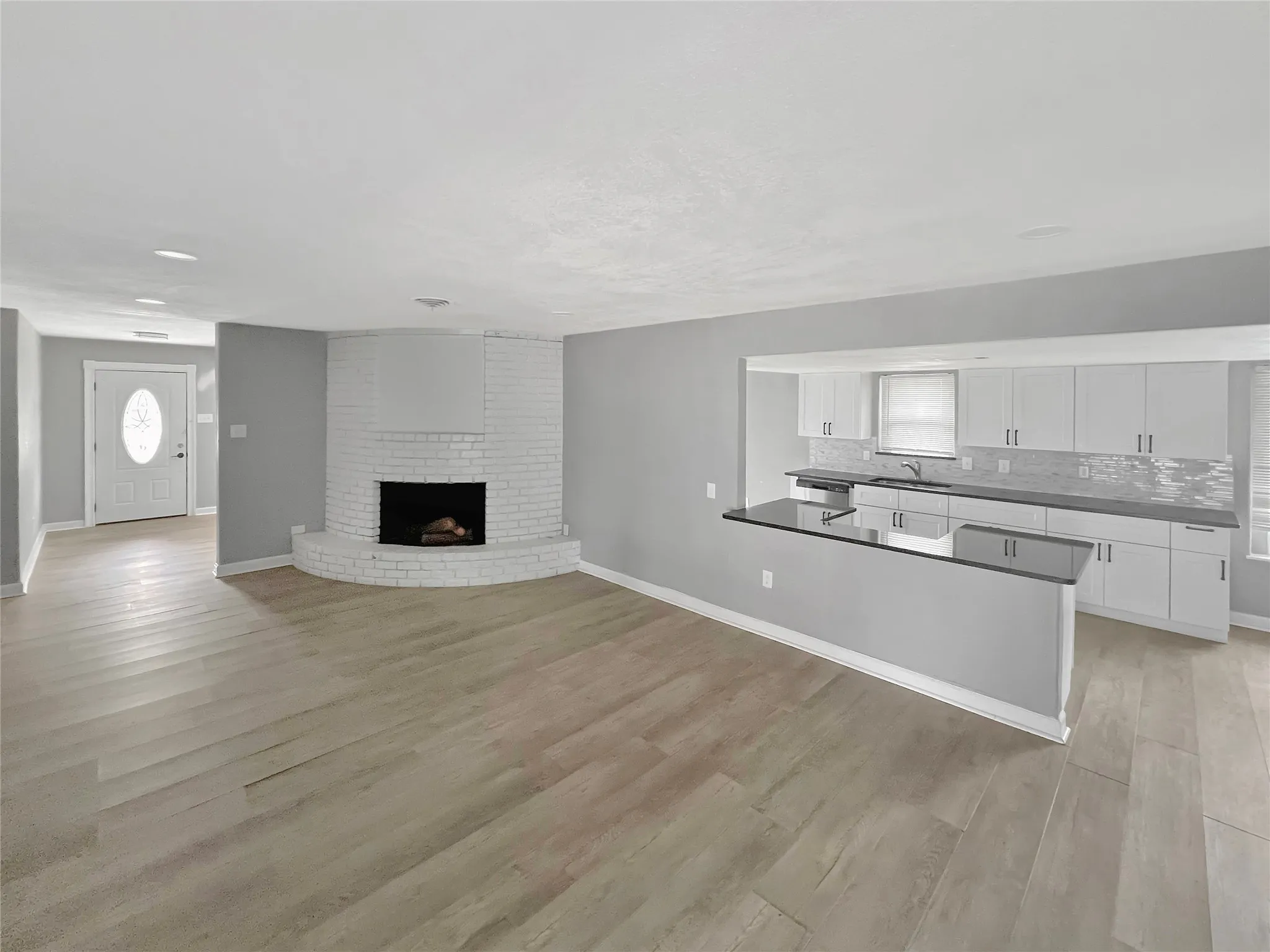 Expansive living space featuring light wood-finish flooring and a white painted brick fireplace