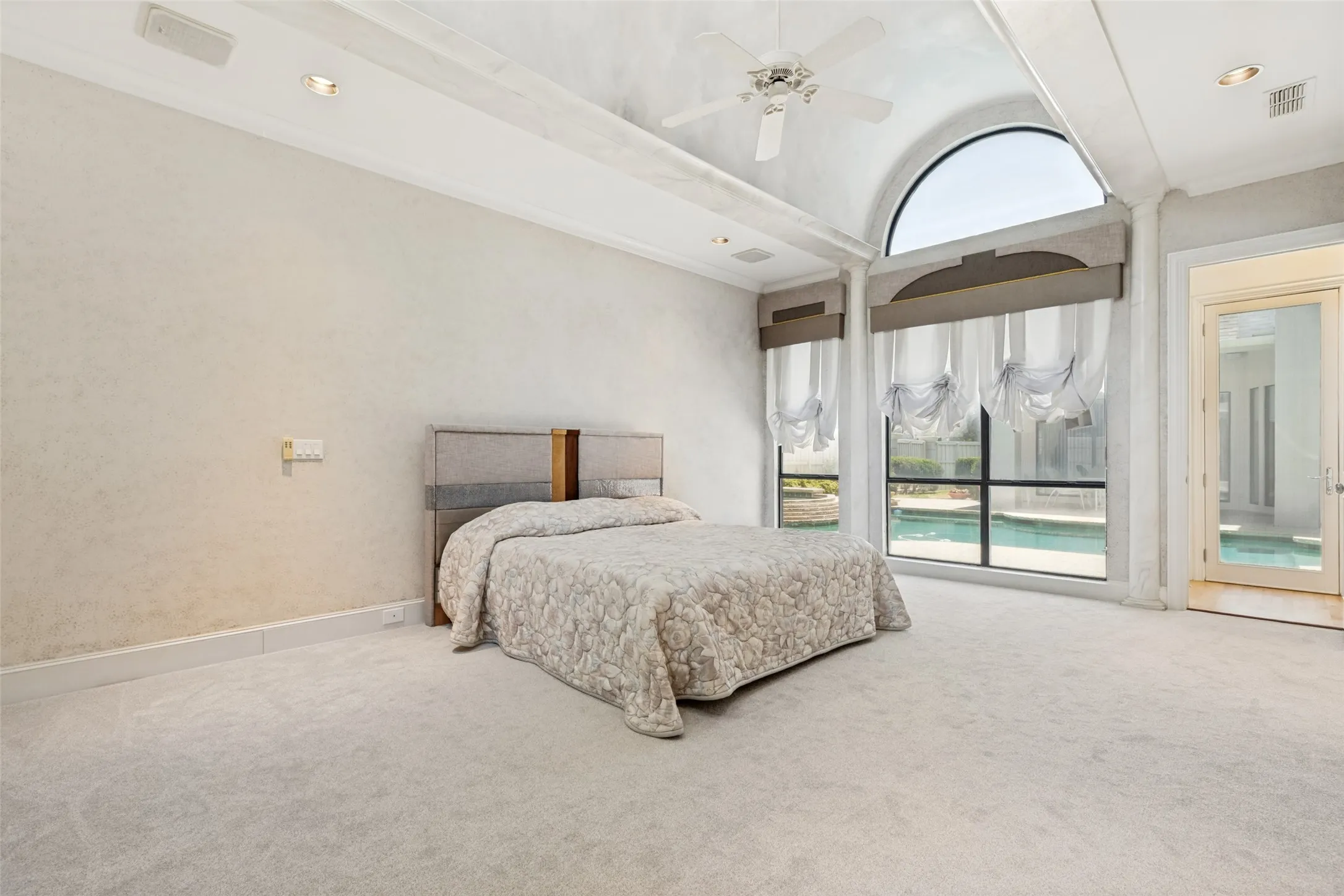 Arched window overlooking a pool, featuring floor-to-ceiling glass, a glass-paneled door, and recessed lighting