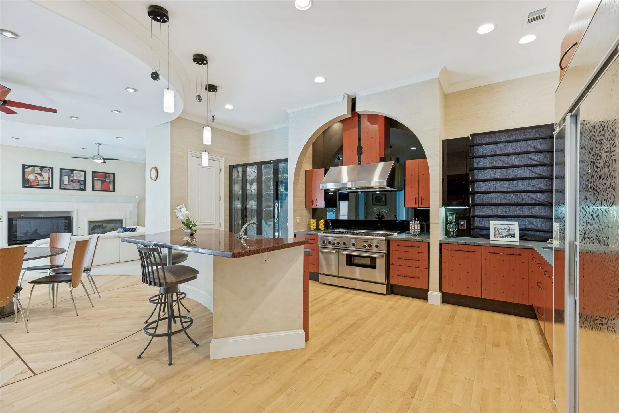 Open-concept kitchen featuring wood-finish flooring, a stainless steel range with a professional hood, and a built-in refrigerator with a frosted glass door