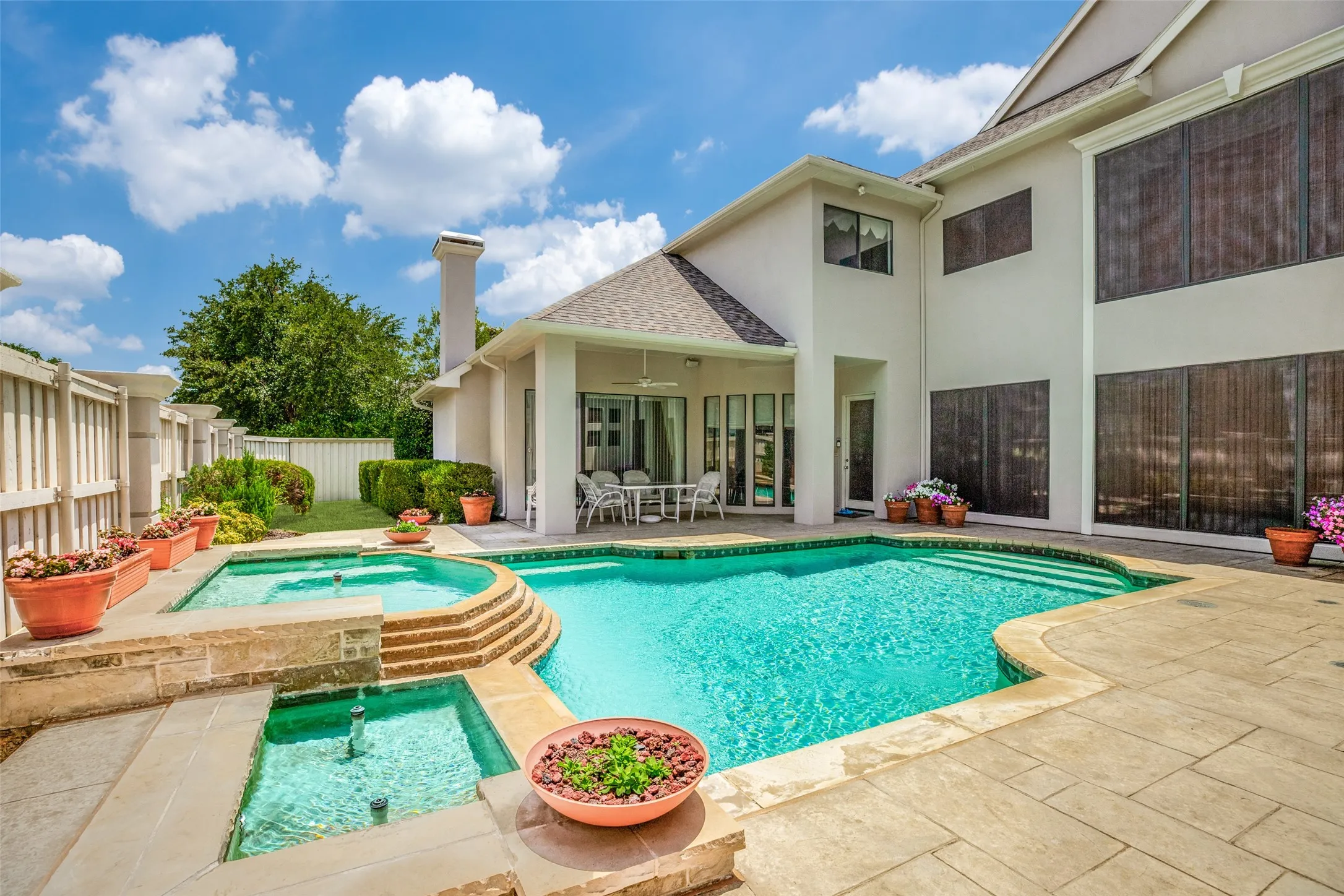 Expansive outdoor living area featuring a large swimming pool with integrated spa, a tiered water feature, and a covered patio