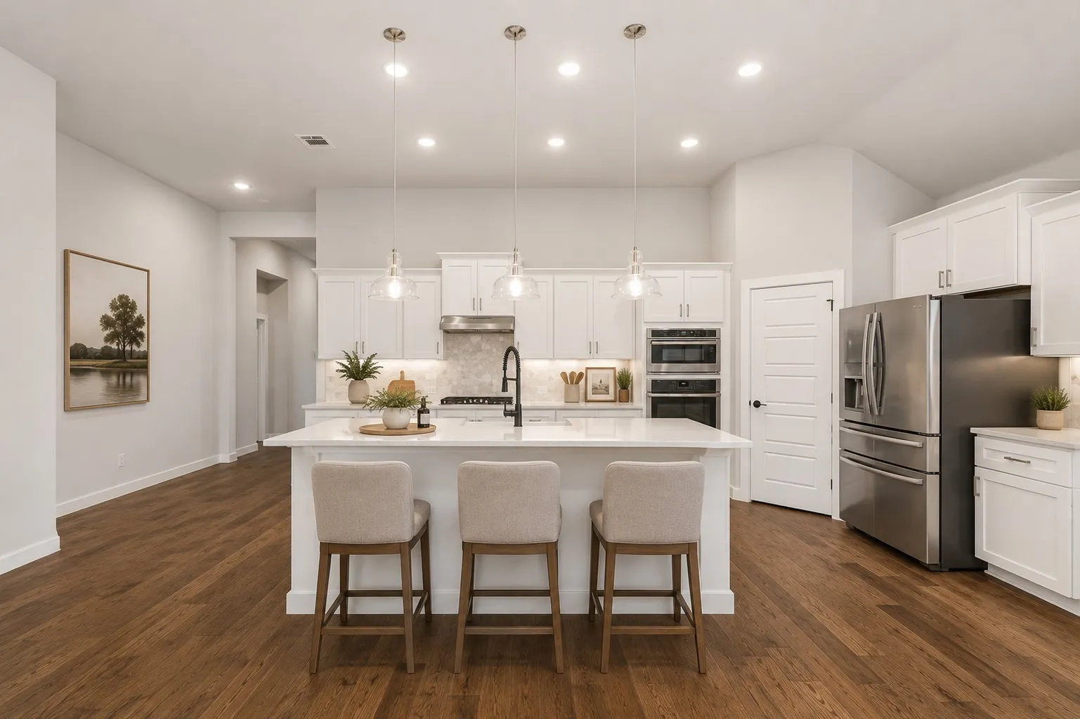Kitchen featuring a large island with three pendant lights, white cabinetry, integrated stainless steel appliances, and wood-finish flooring