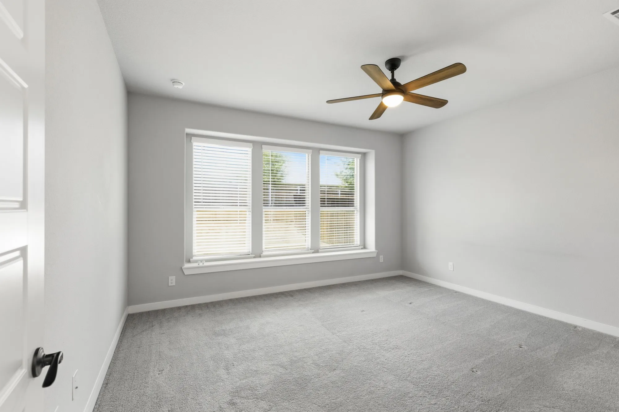 Room featuring light gray carpeting, neutral wall paint, and a ceiling fan with wood-finish blades