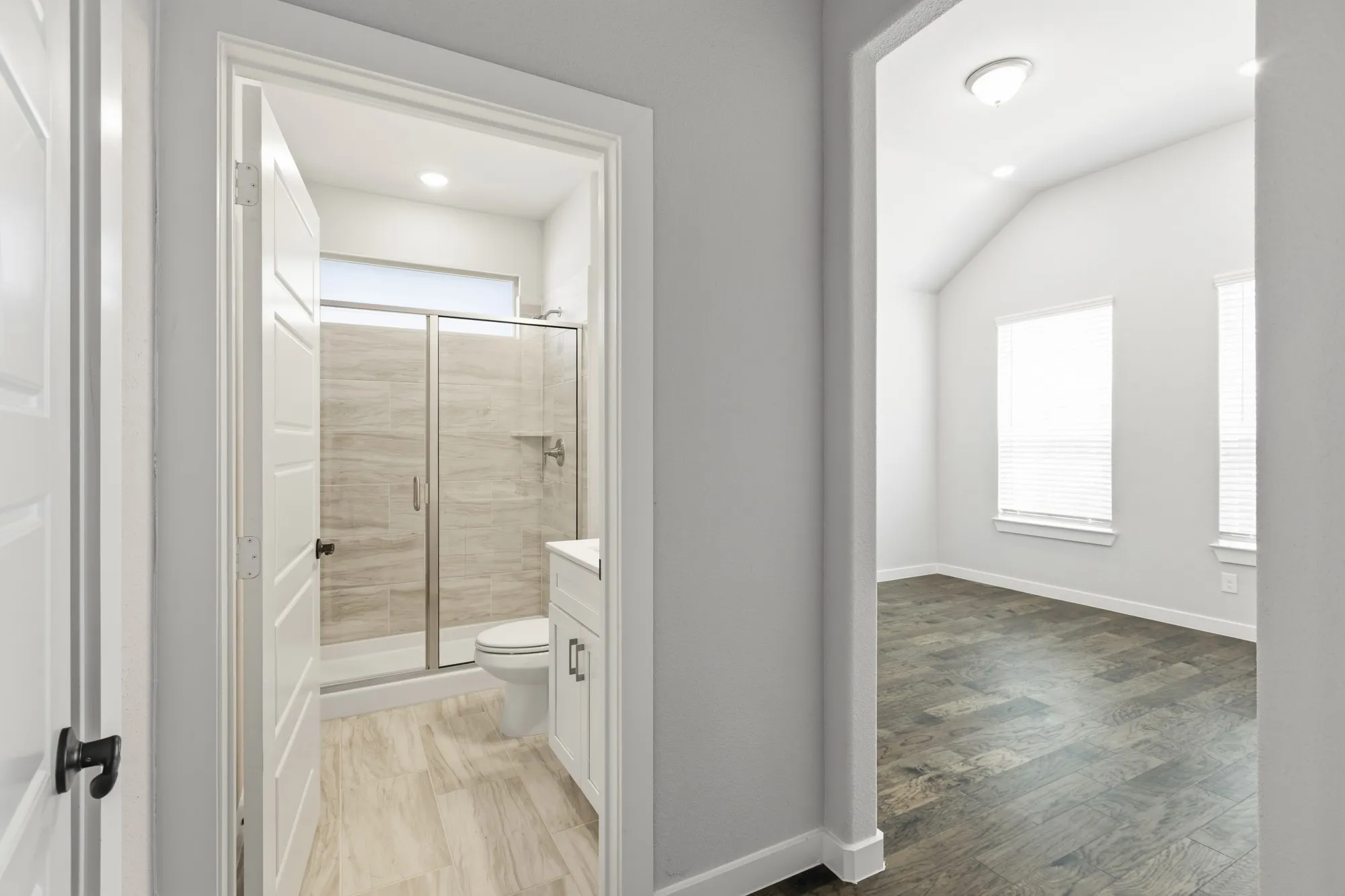 Modern bathroom featuring a glass-enclosed shower with tile surround, white vanity, and wood-finish flooring