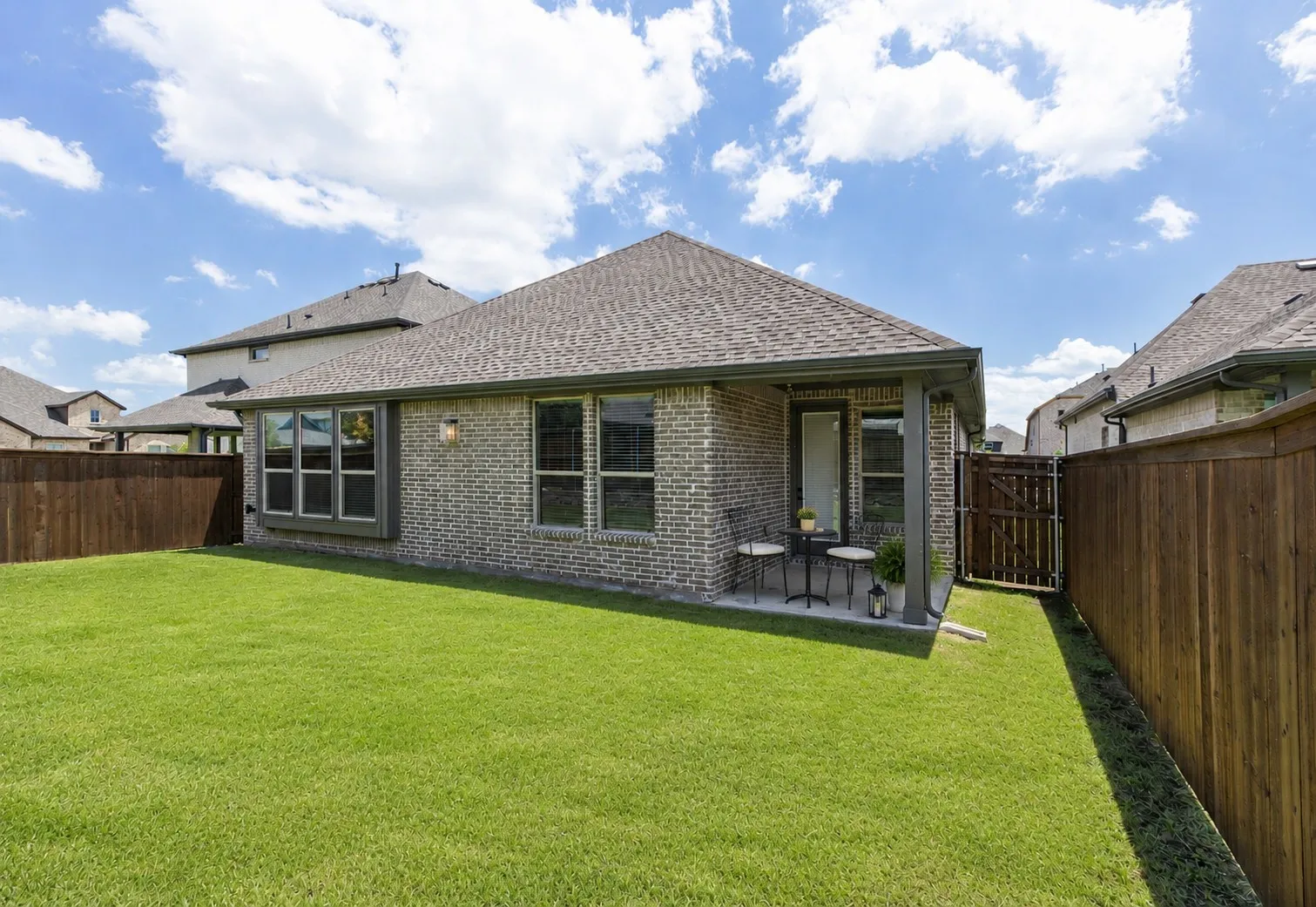 Expansive backyard featuring a manicured lawn, full privacy fencing, a covered patio, and a brick exterior with multiple windows
