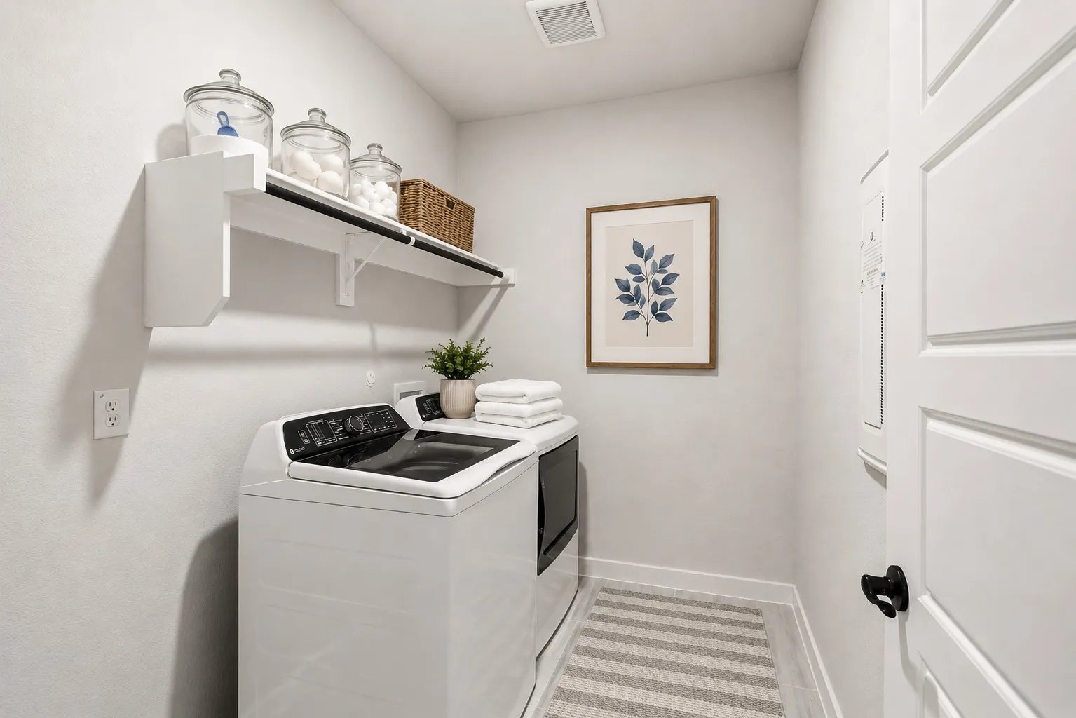 Dedicated utility space featuring a top-load washing machine, built-in shelving, white paneled door, light-toned wall paint, and wood-finish flooring