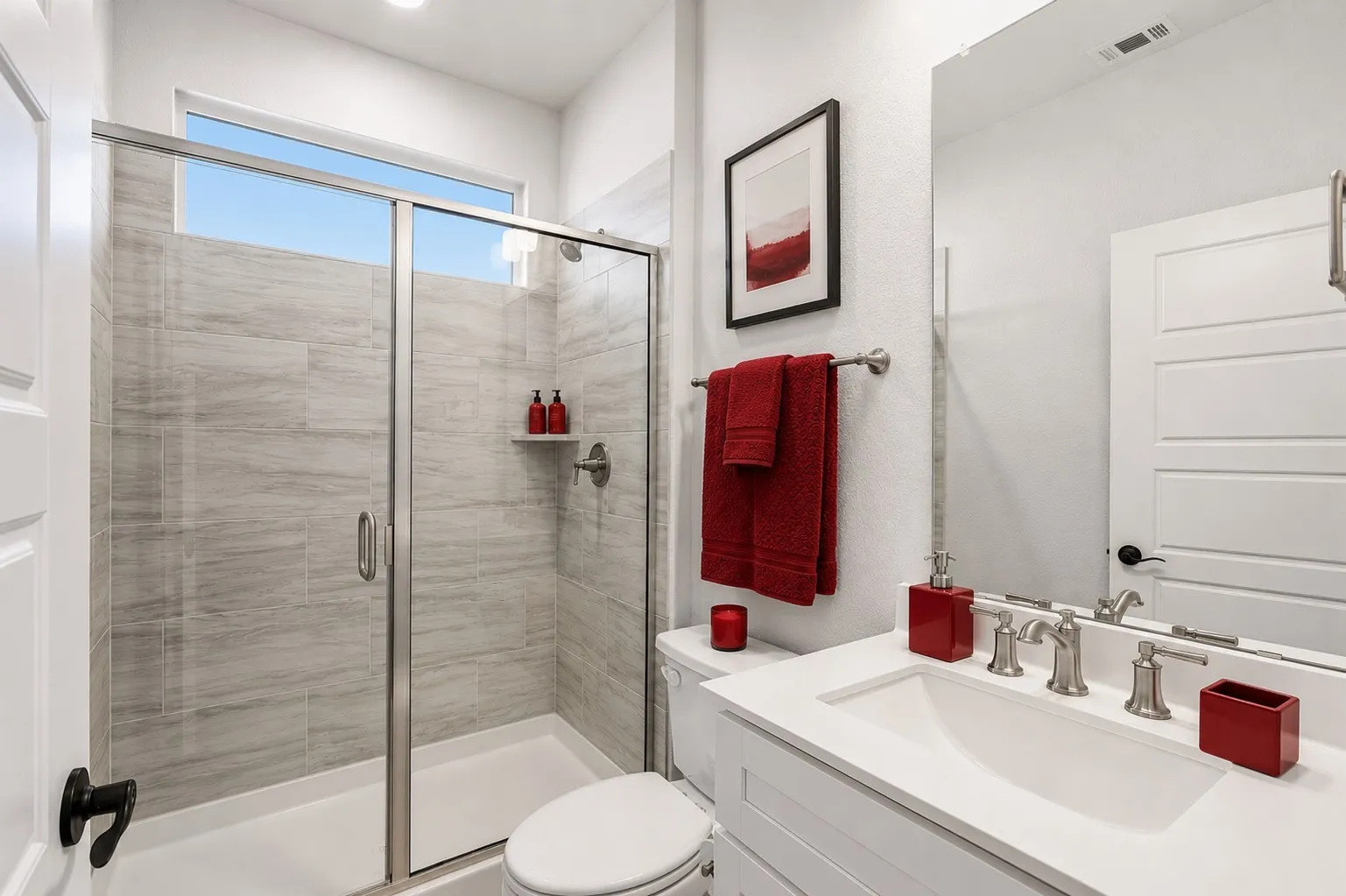 Shower with glass enclosure and light-hued tile surround, featuring a built-in shelf