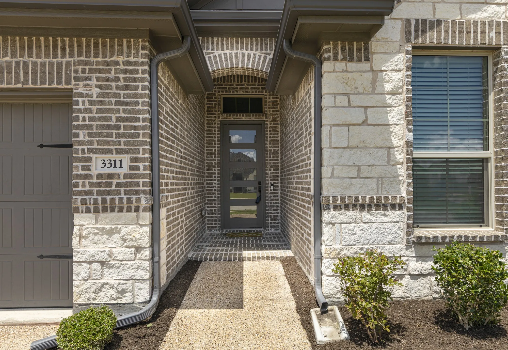 Modern exterior featuring a brick and stone facade, covered entryway, and a contemporary glass-paneled front door