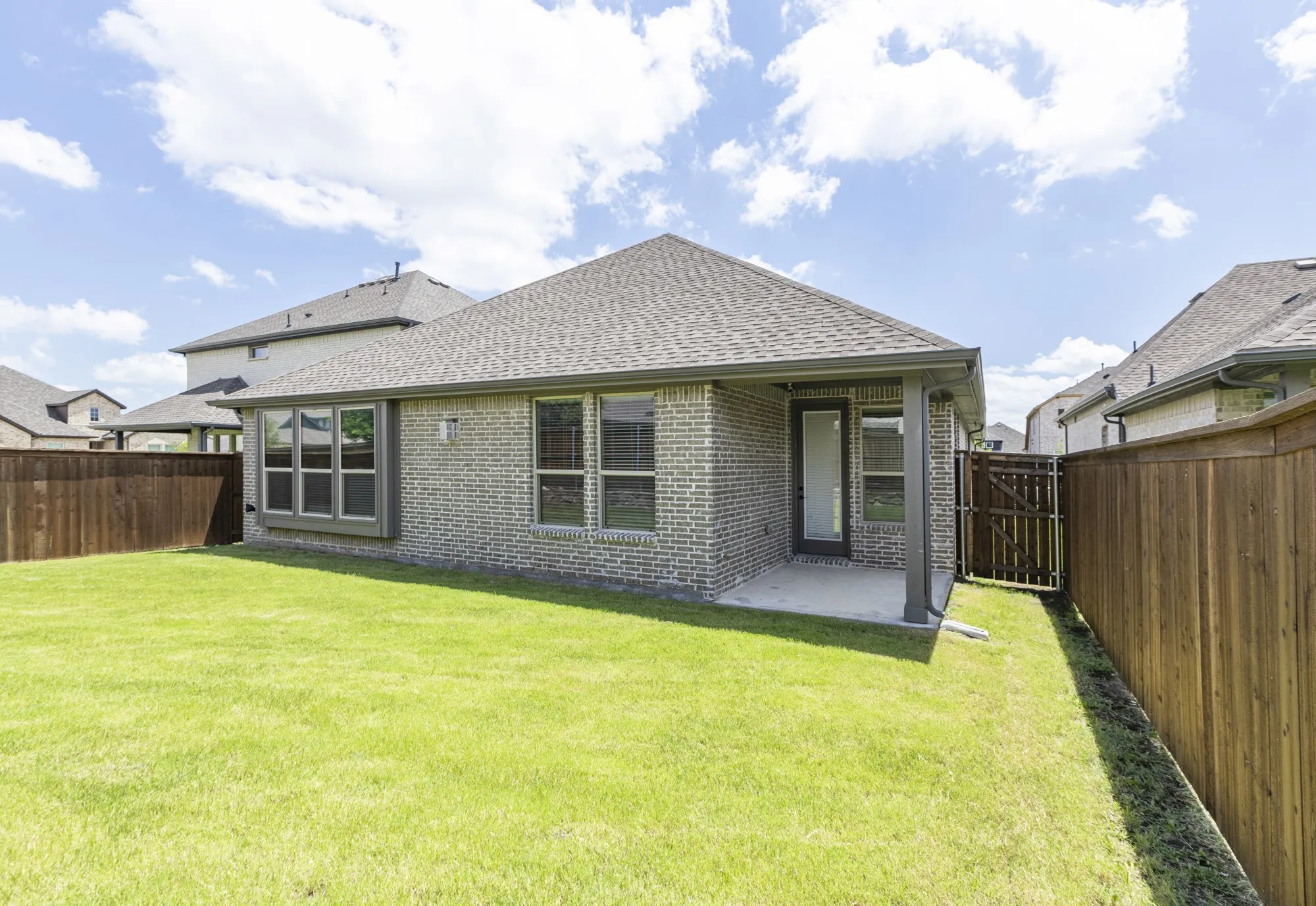 Expansive backyard featuring a manicured lawn, full privacy fencing, and a covered patio with direct access to the interior