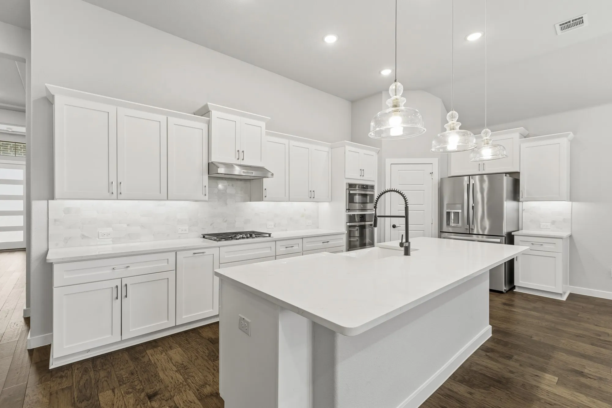 Contemporary kitchen featuring white cabinetry, a large center island with a black gooseneck faucet, stainless steel appliances, and wood-finish flooring