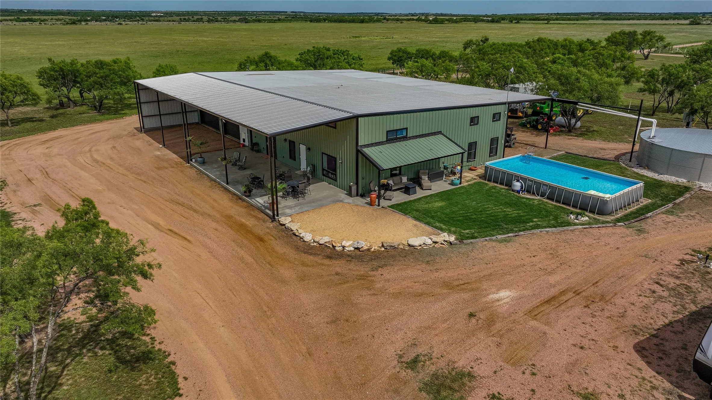 Aerial view of a 283.98 acre Rochelle, Texas ranch for sale in McCulloch County. The 2023 barndominium has a wraparound covered patio, pool, rainwater collection tank and open hay fields.