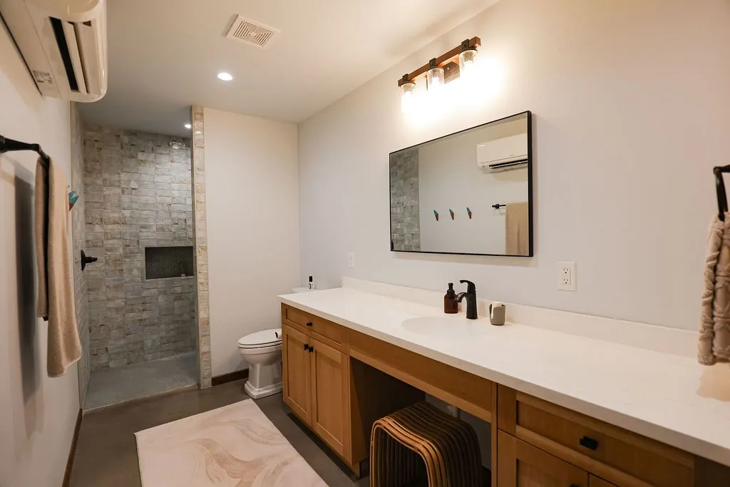 Spacious bathroom with a doorless walk in shower wrapped in textured tile, a built in niche and an extended quartz vanity with a seated makeup area. It's a clean, modern bath inside this Texas ranch home.