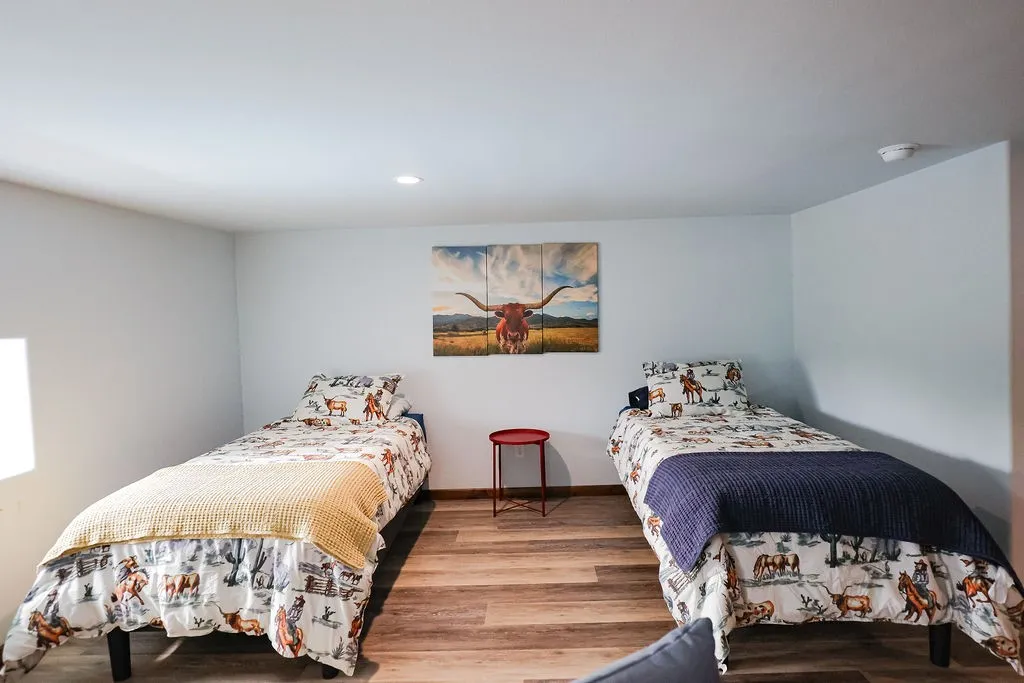 Spacious bunk room with two twin beds, luxury vinyl plank floors and recessed lighting. It's ready for hunting buddies, guests or retreat stays at this Texas ranch lodge.