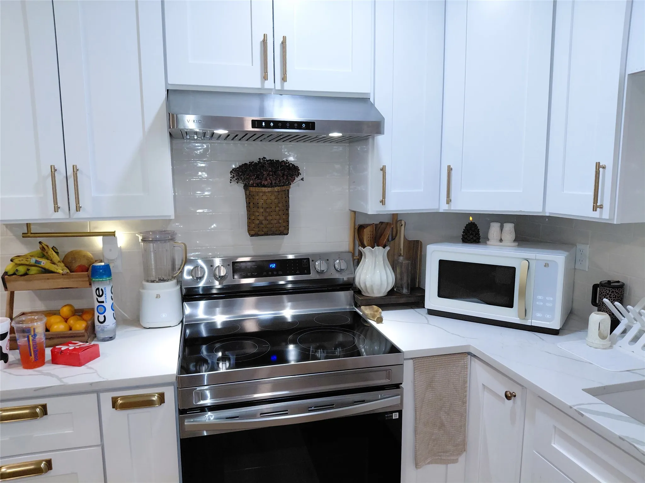 White shaker cabinetry with gold-finish hardware, stainless steel range, white subway tile backsplash, and light-tone countertops