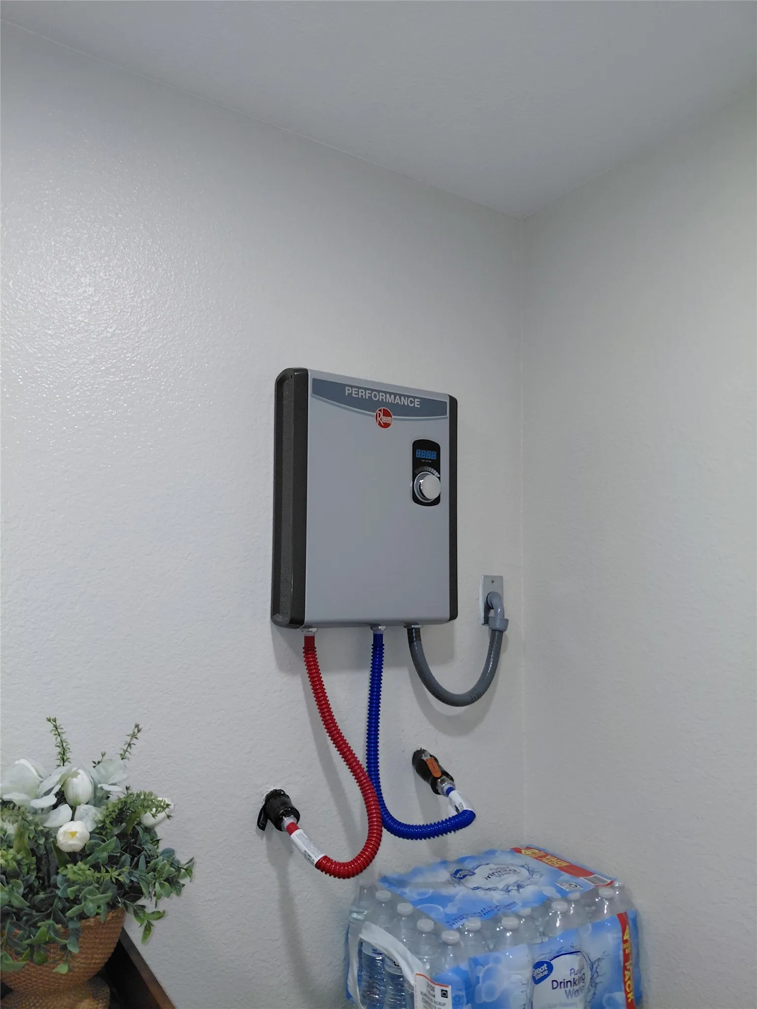 Wall-mounted tankless water heater with visible controls and connected hoses