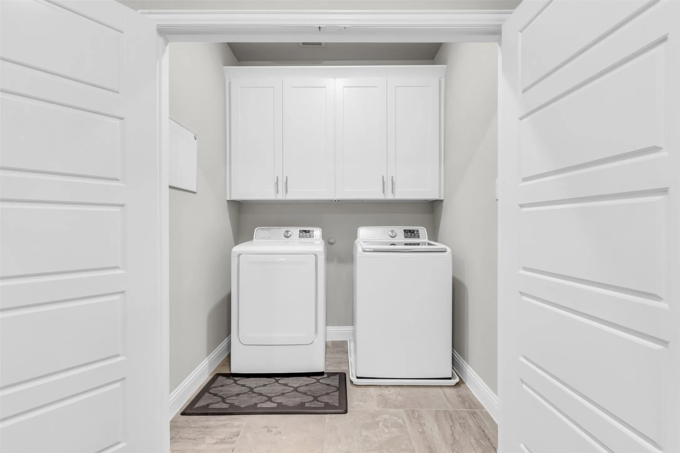 Dedicated laundry area featuring white shaker-style cabinetry with brushed nickel hardware, light grey wall paint, and wood-finish flooring