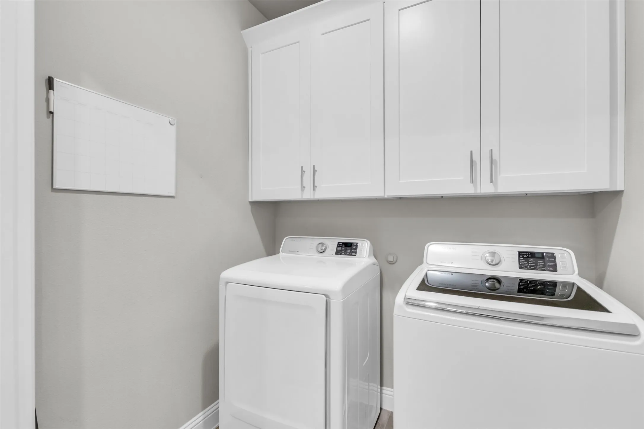 Utility room featuring white shaker-style cabinetry with brushed nickel hardware, and wood-finish flooring