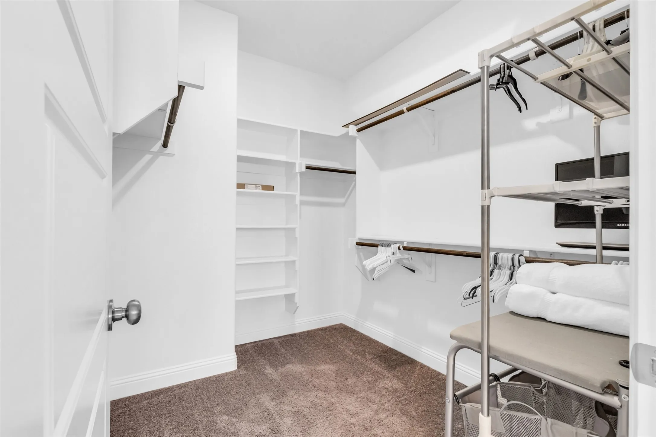 Walk-in closet with carpet flooring, white baseboards, multiple built-in shelving units, and hanging rods