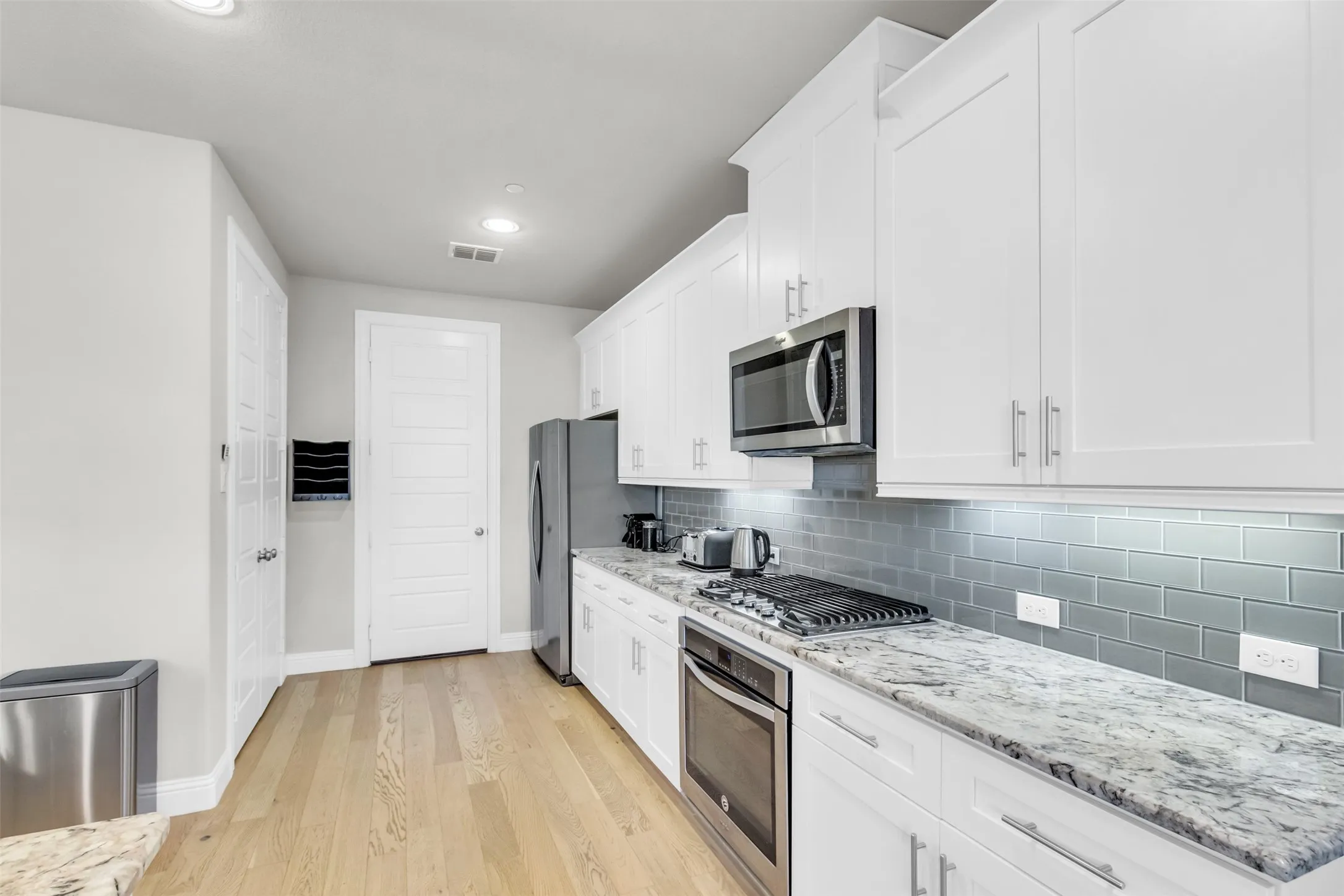 Kitchen featuring white shaker cabinetry, stainless steel appliances, light-toned wood-finish flooring, a gas range, and a subway tile backsplash