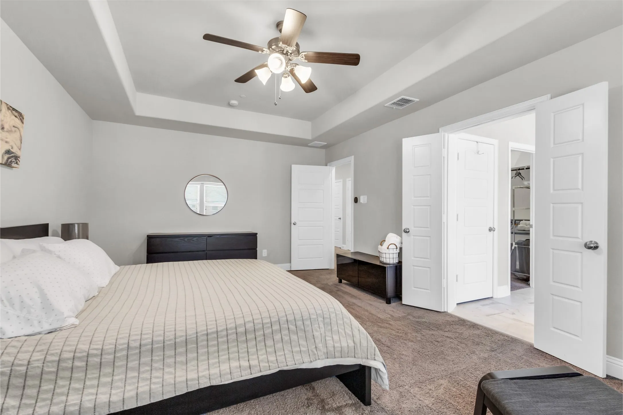 Spacious interior featuring a tray ceiling with a ceiling fan, light gray wall paint, and a circular wall mirror