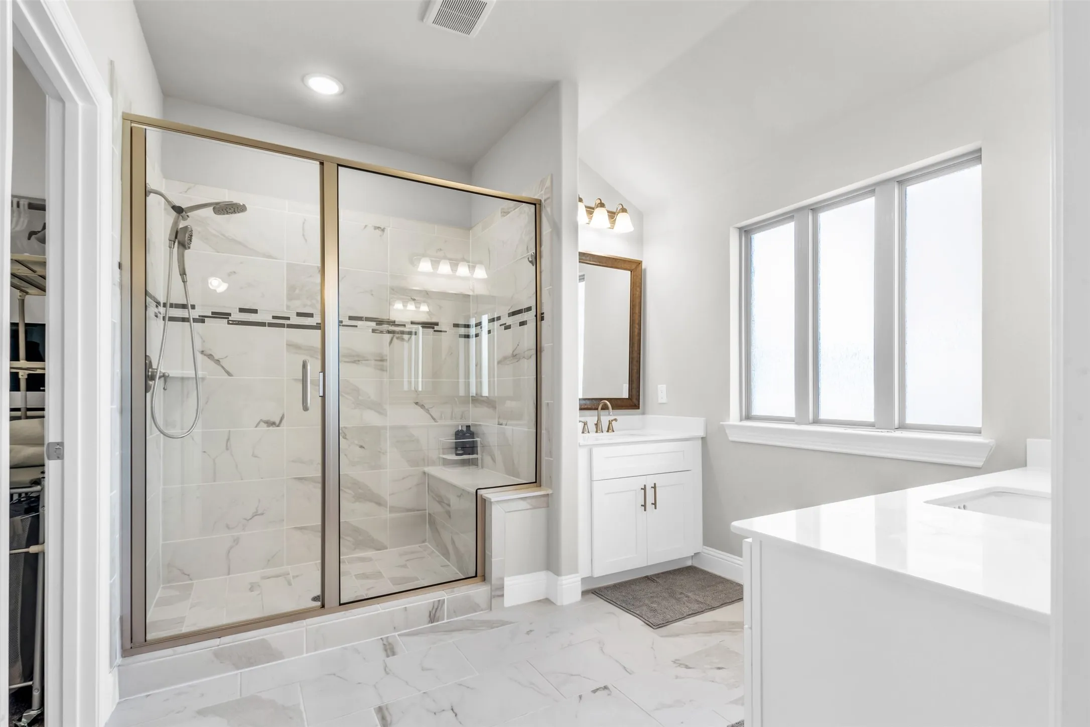 Spacious bathroom featuring a glass-enclosed shower with a built-in bench, marble-finish tile, and a dual shower head