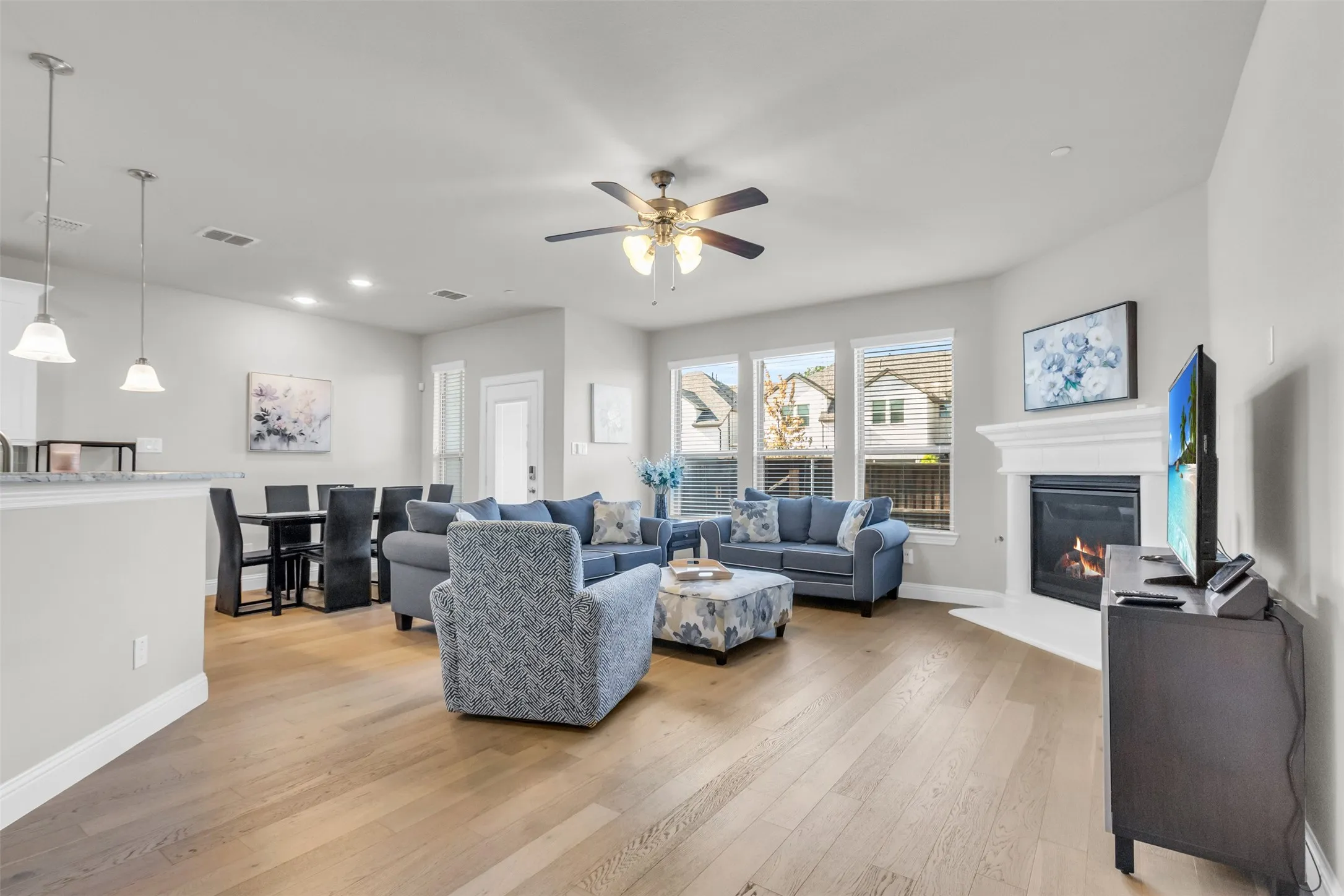 Open-concept living space featuring wood-finish flooring, a contemporary fireplace with a white mantel, and multiple large windows