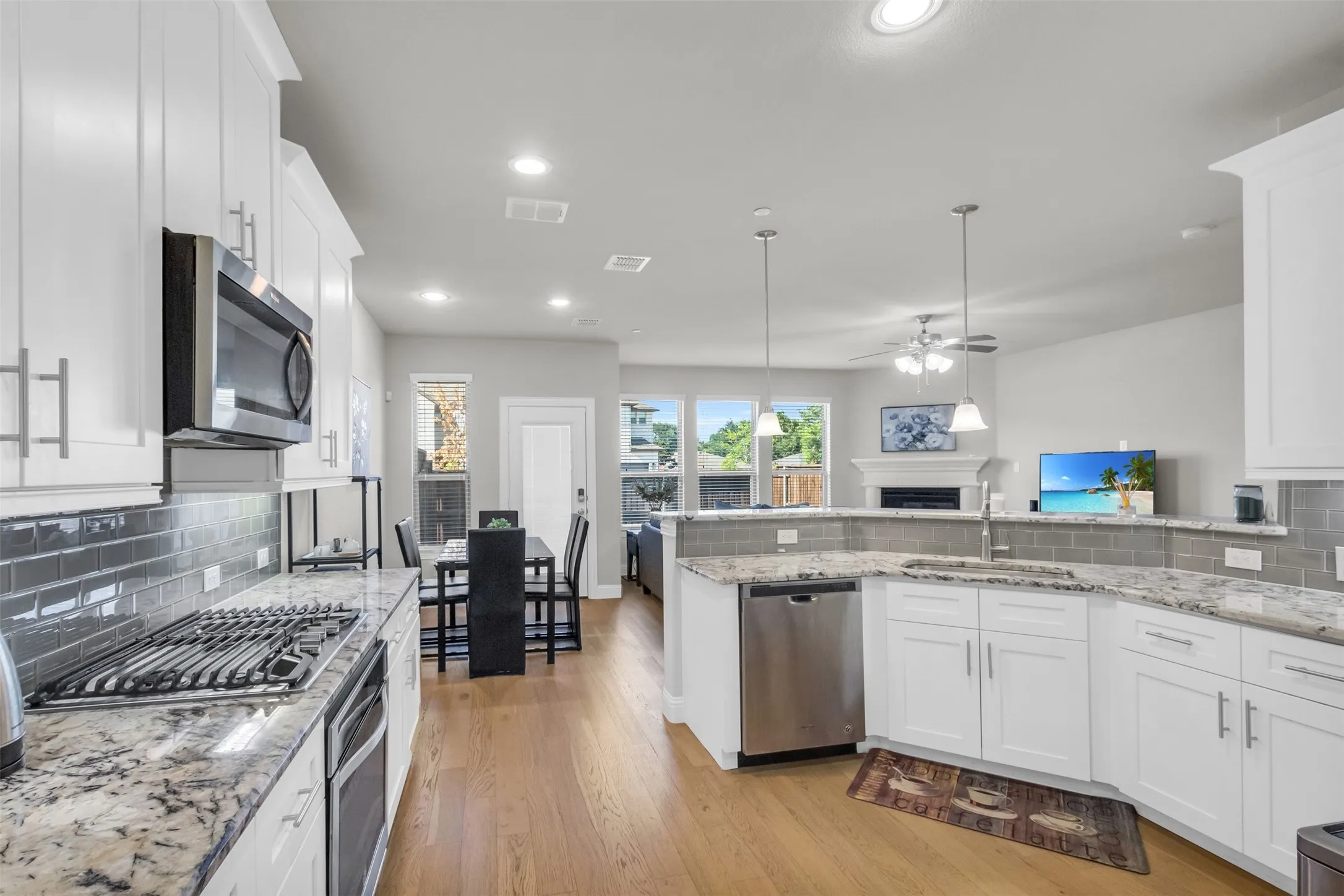 Open-concept kitchen featuring white cabinetry, stainless steel appliances, granite countertops, a subway tile backsplash, and wood-finish flooring