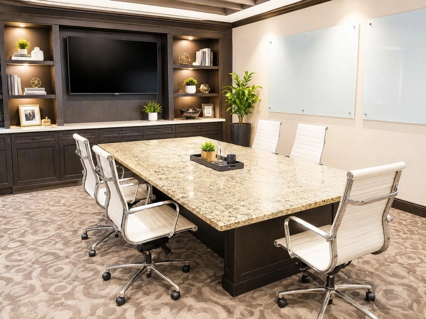 Spacious meeting room featuring a granite-topped conference table, custom built-in cabinetry with integrated shelving and lighting, and dual wall-mounted presentation boards