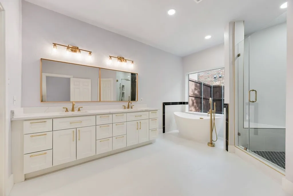 Indulge in the spa-inspired primary bath featuring dual vanities, elegant gold fixtures, freestanding soaking tub