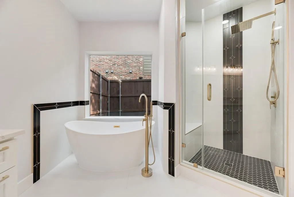 Indulge in the spa-inspired primary bath including elegant gold fixtures, freestanding soaking tub, walk-in-shower with designed tile.
