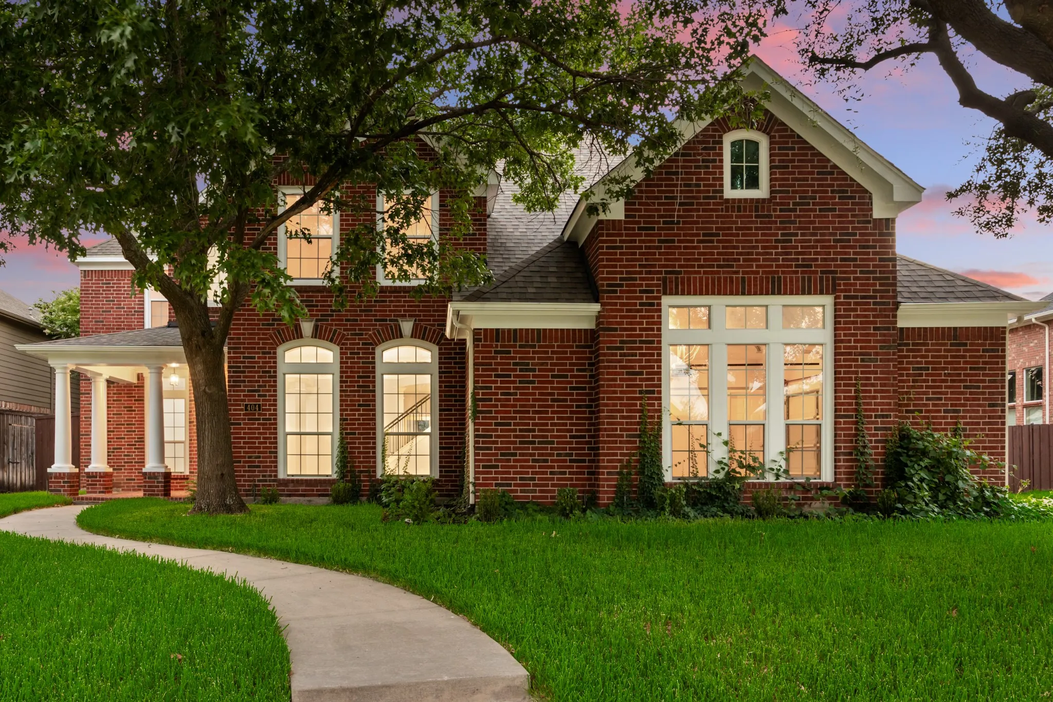 Red brick exterior featuring a covered entry with columns, multiple arched windows, a front gable, and a winding concrete pathway