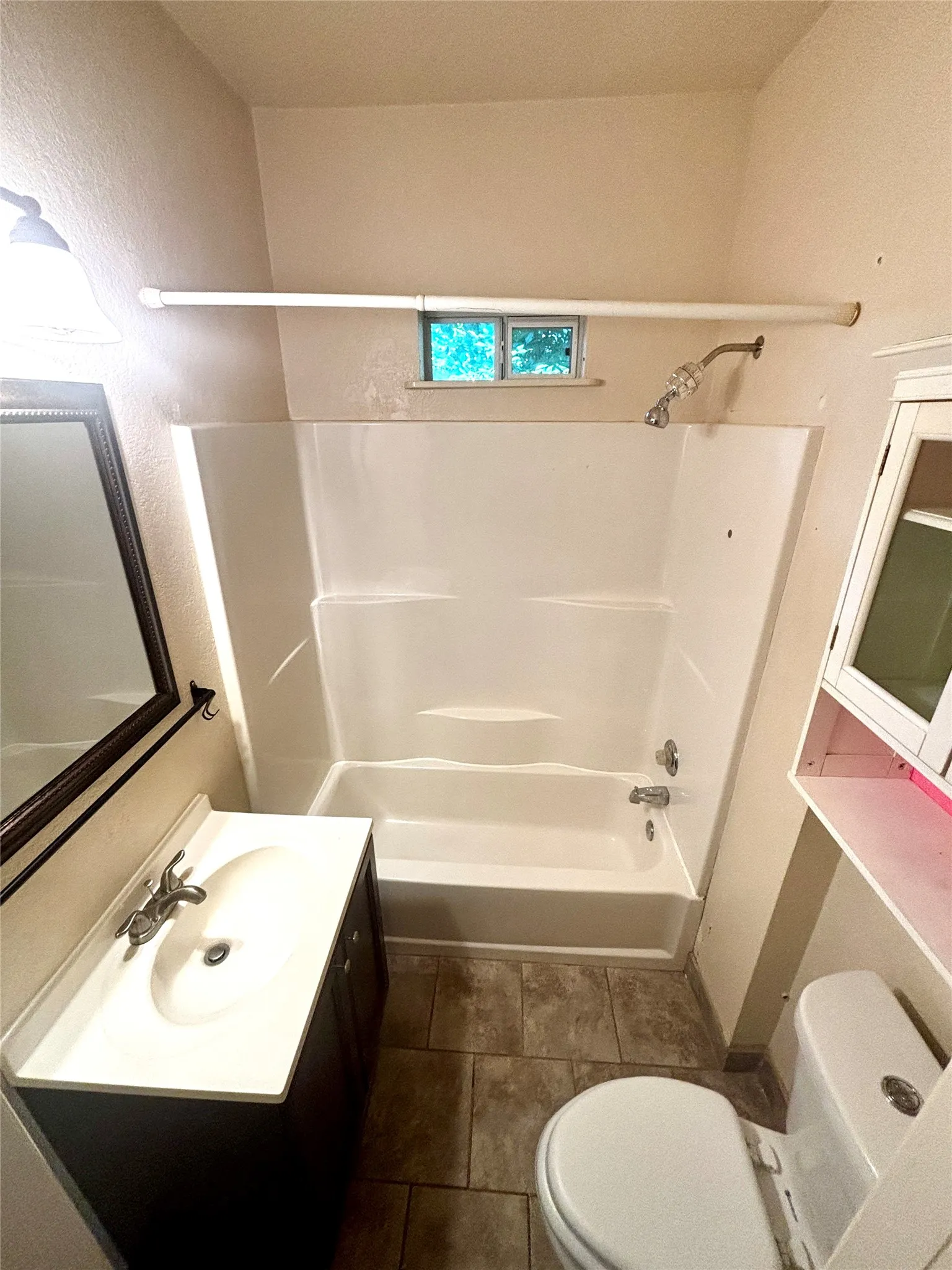 Bathroom featuring a built-in shower/tub combination with a window, a vanity with an integrated sink, a toilet, and tile flooring