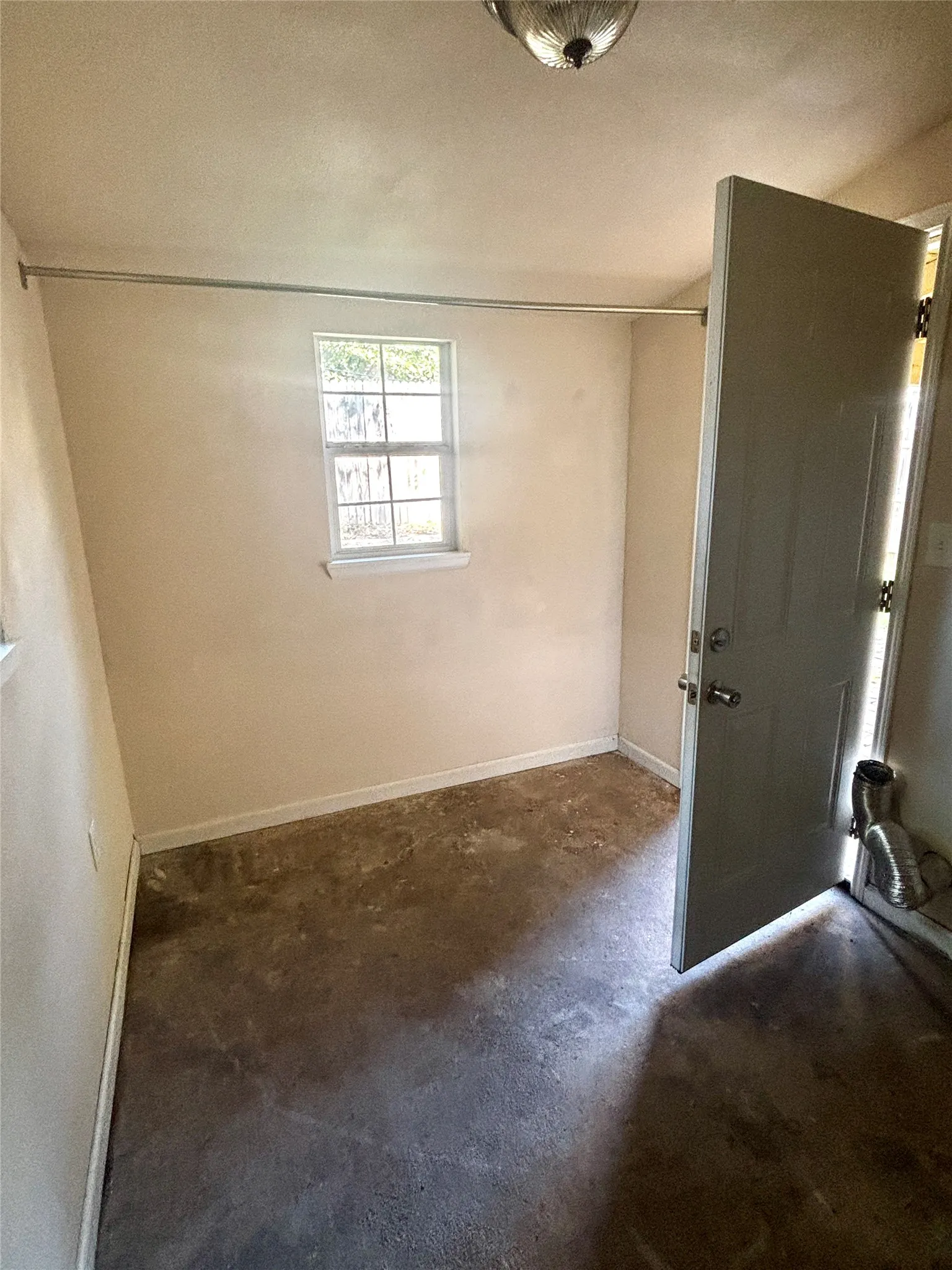 Compact interior room featuring a single window, a light-toned door with a handle, and an overhead light fixture