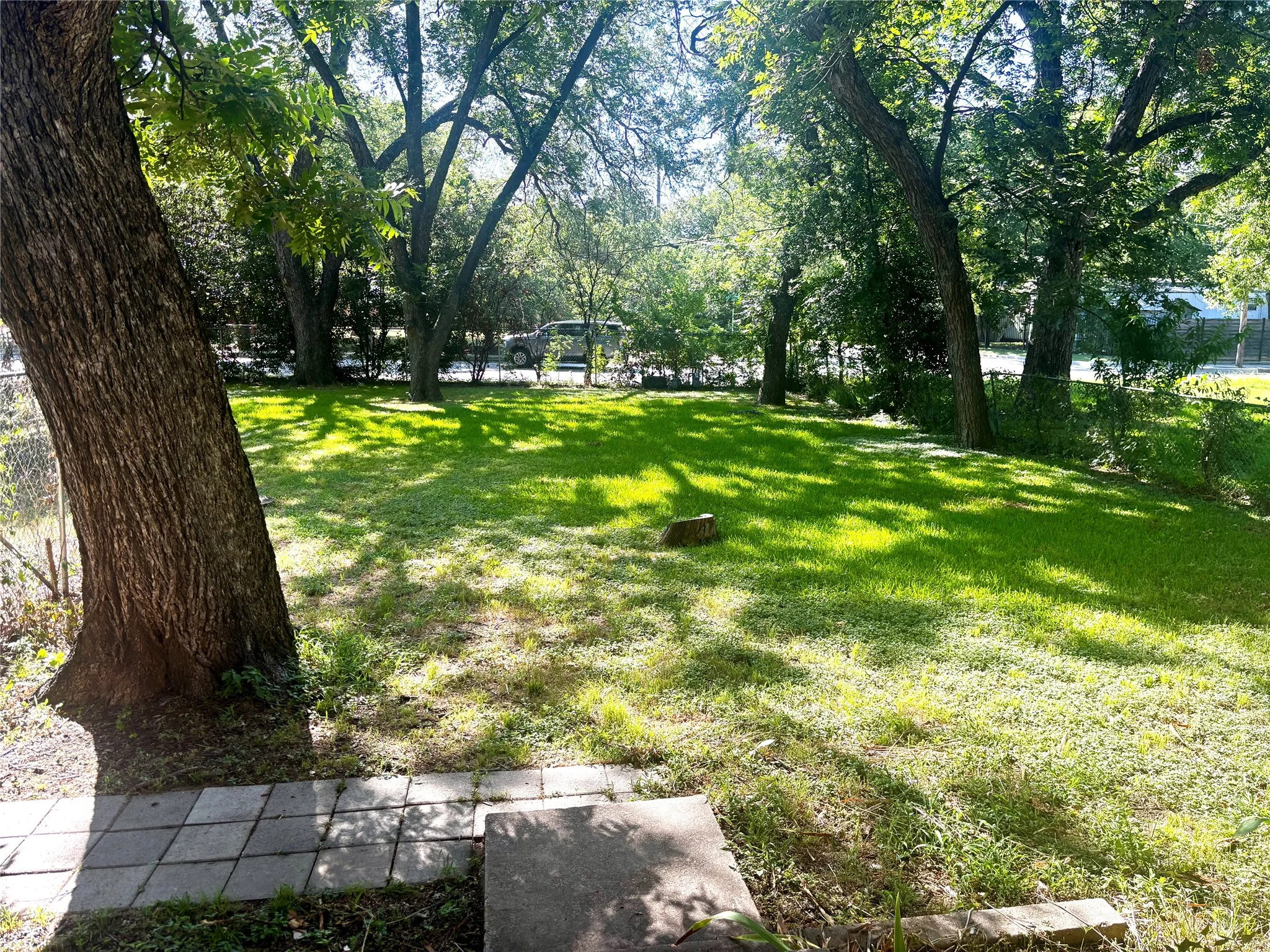 Fenced in front yard .featuring mature trees providing ample shade, a manicured lawn, and a partial chain-link fence