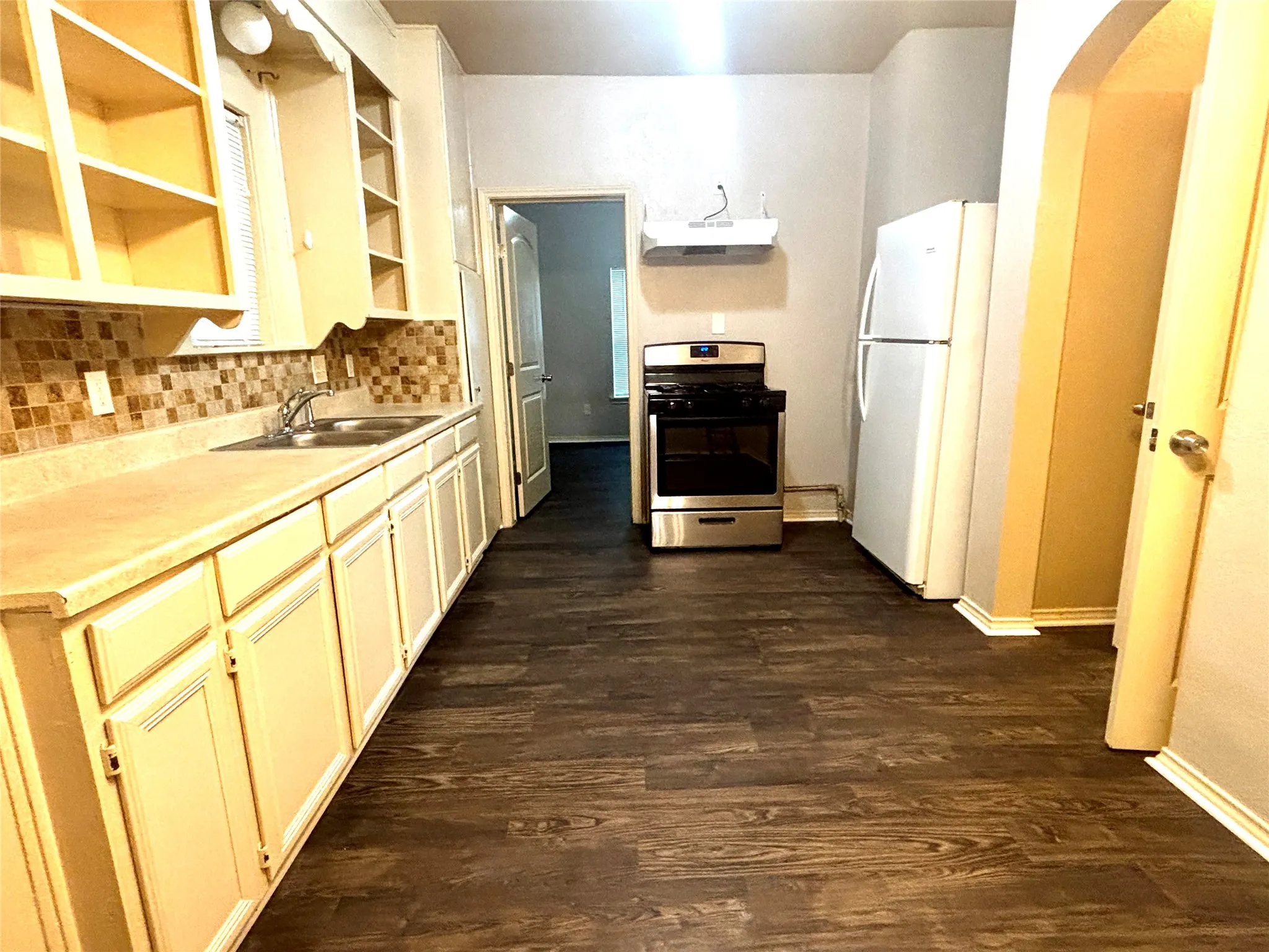 Kitchen featuring dark wood-finish flooring, light cabinetry with decorative trim, a mosaic tile backsplash, double basin sink, and stainless steel range