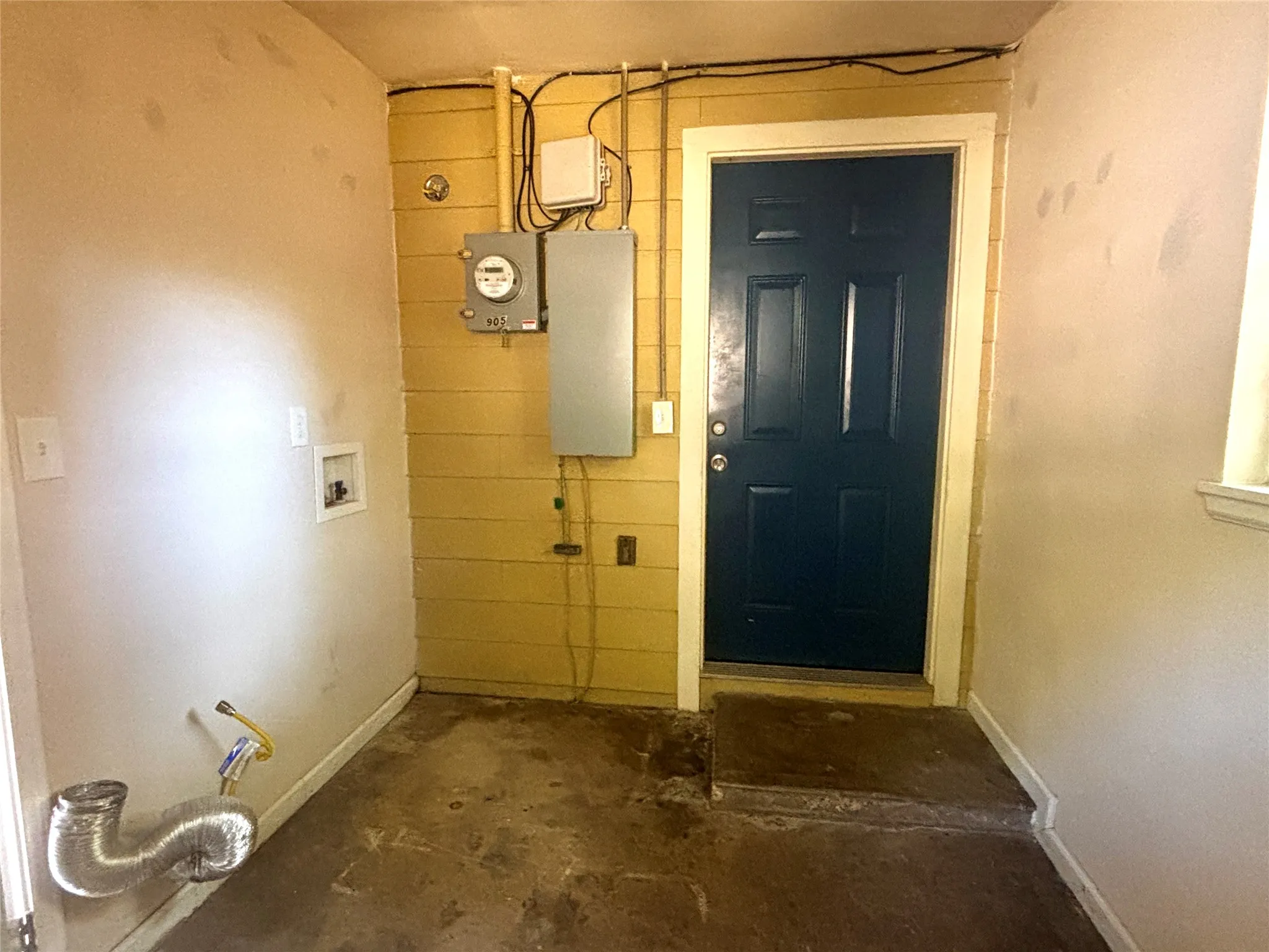 Laundry area with utility hookups, a dark paneled door, and a concrete floor