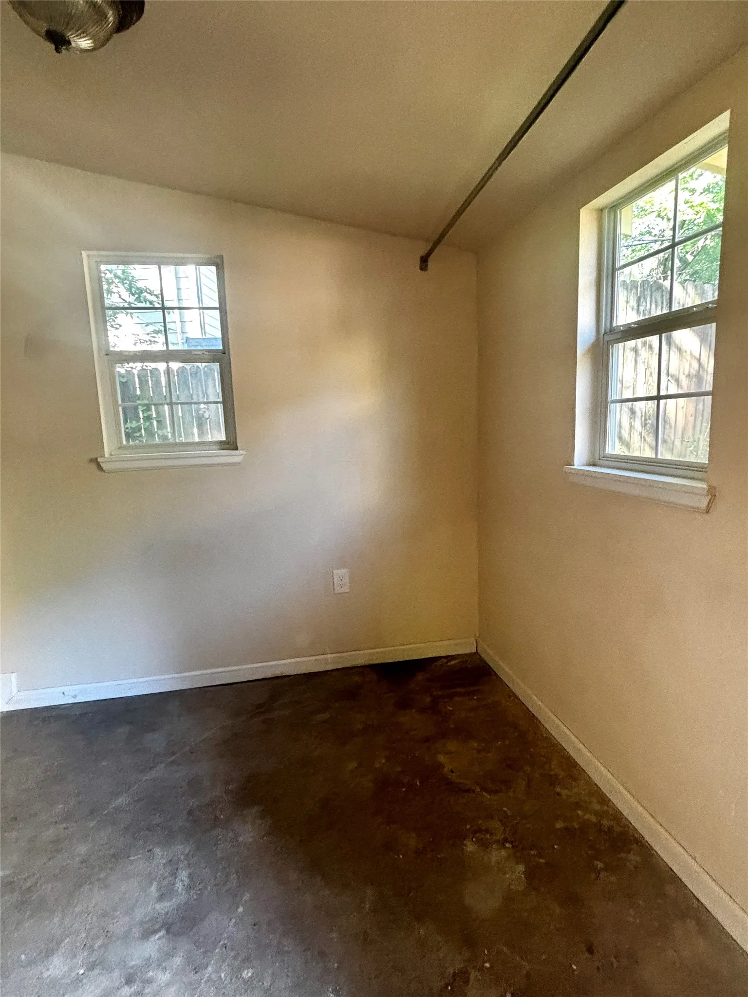 Room featuring two double-hung windows, light-toned walls, and a dark concrete floor