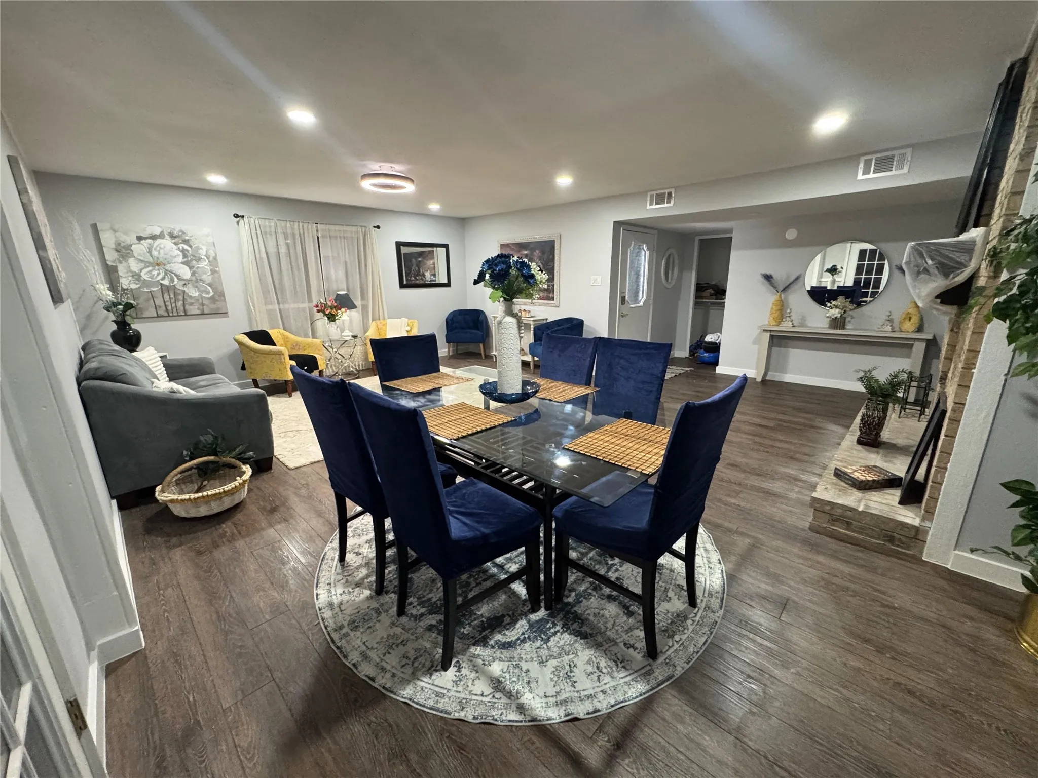 Open-concept living area featuring wood-finish flooring, recessed lighting, and a prominent brick fireplace